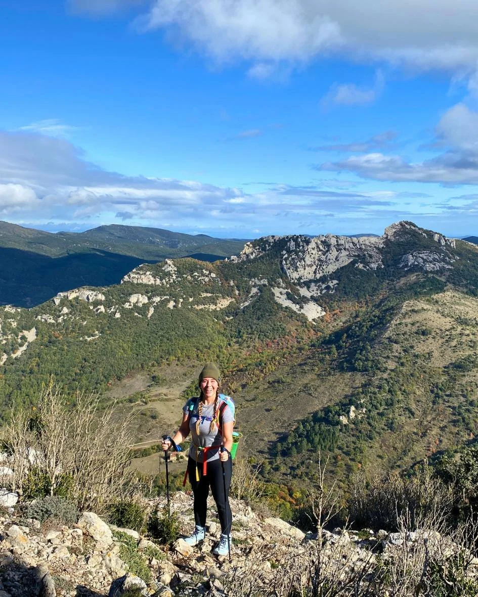Smiling woman standing on the top of a mountain with her hiking polls and backpack.