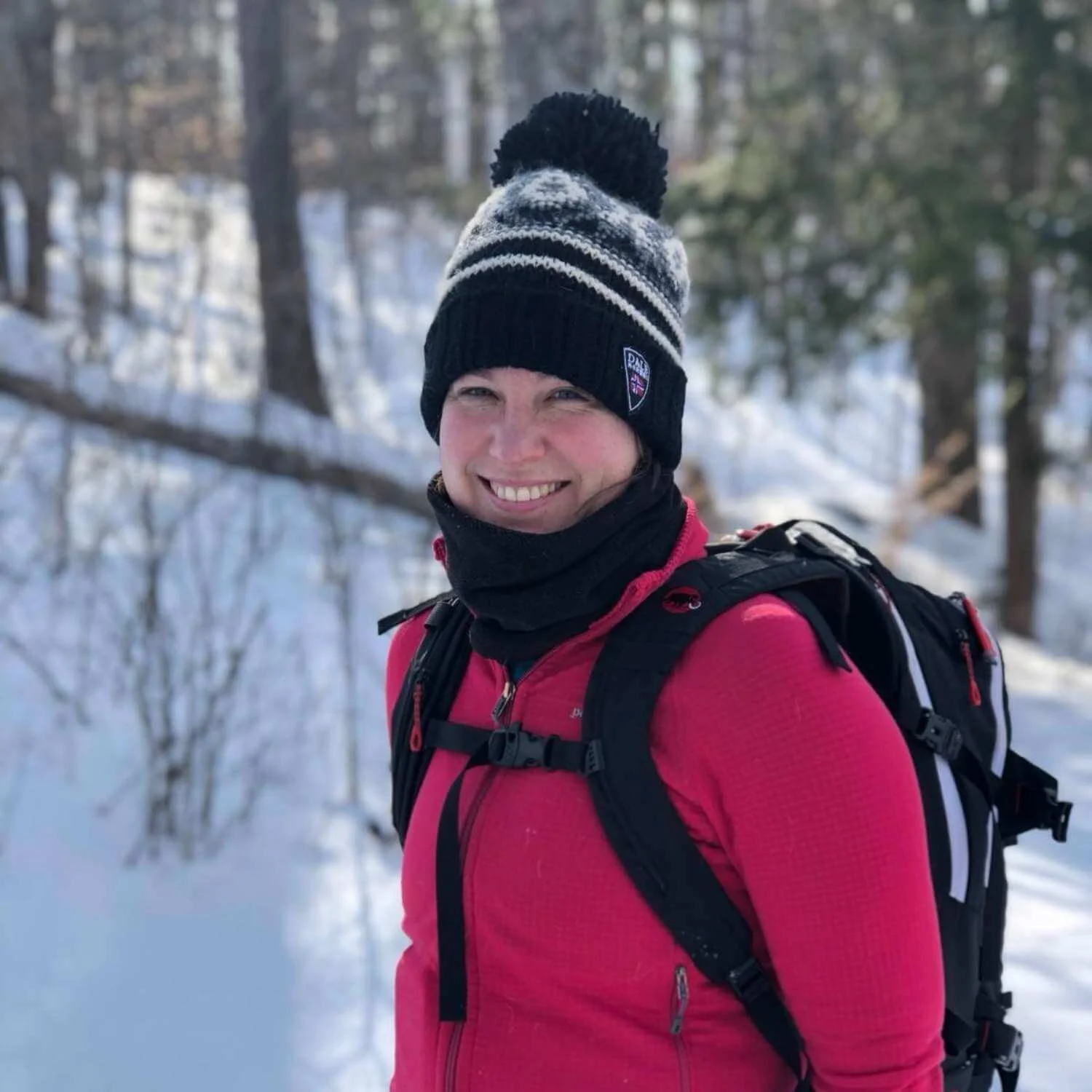 Anna on a snowy woodland trail during an Athara retreat in Europe, wearing a winter hat and backpack.