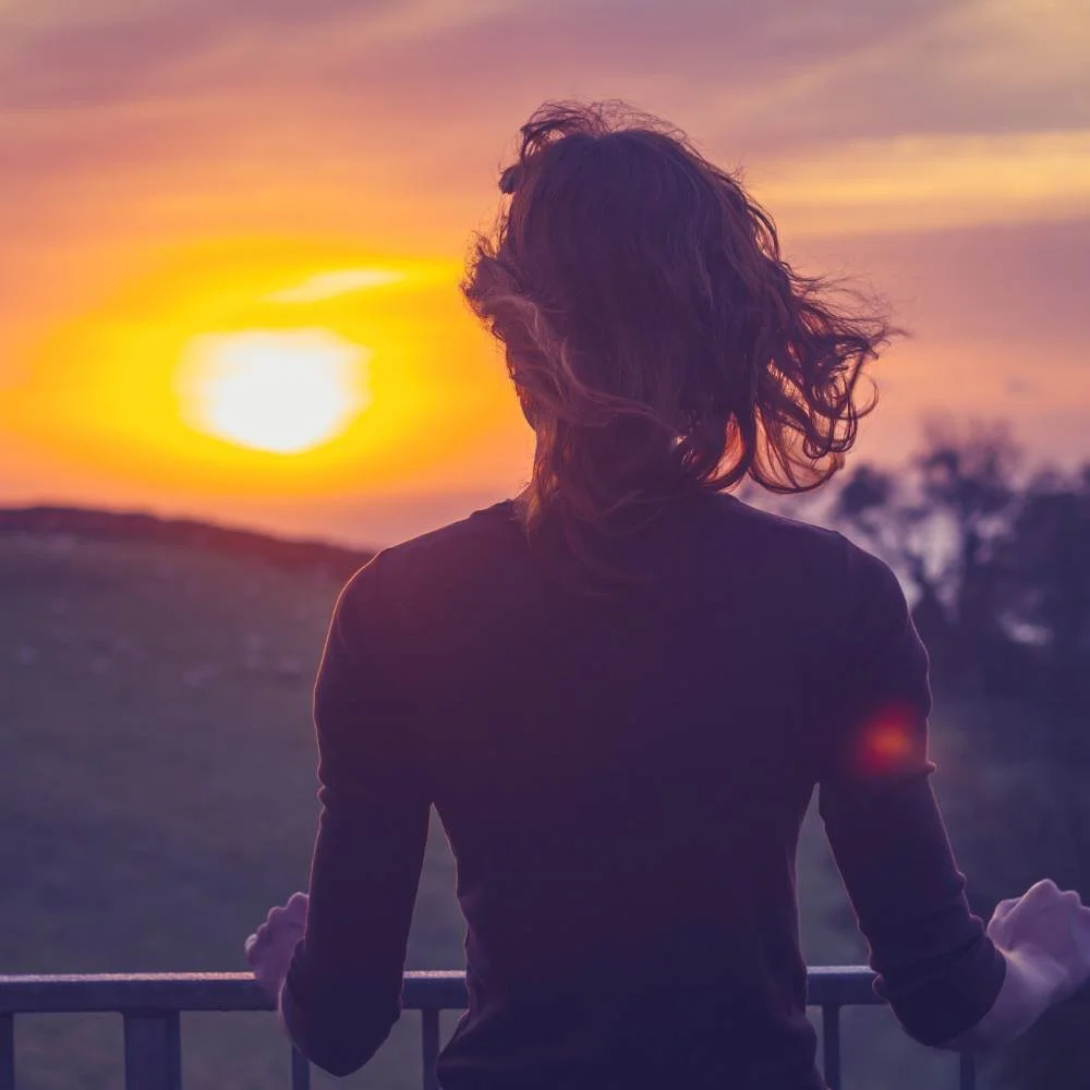 Woman standing at a balcony looking at the sunset.