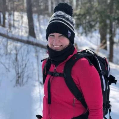 Anna, co-founder of Athara Adventures, standing on a snowy forest trail during an Athara retreat in Europe, wearing a winter hat and backpack.