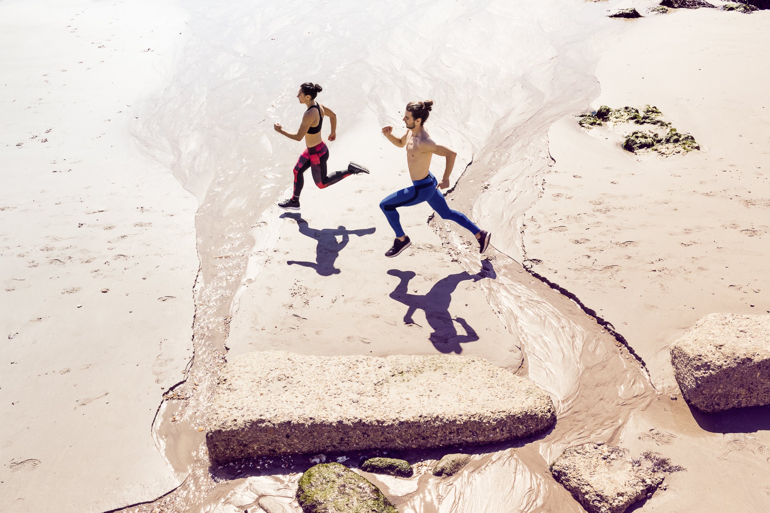 A lifestyle action shot of runners wearing sportswear, running across the sand on a beach.