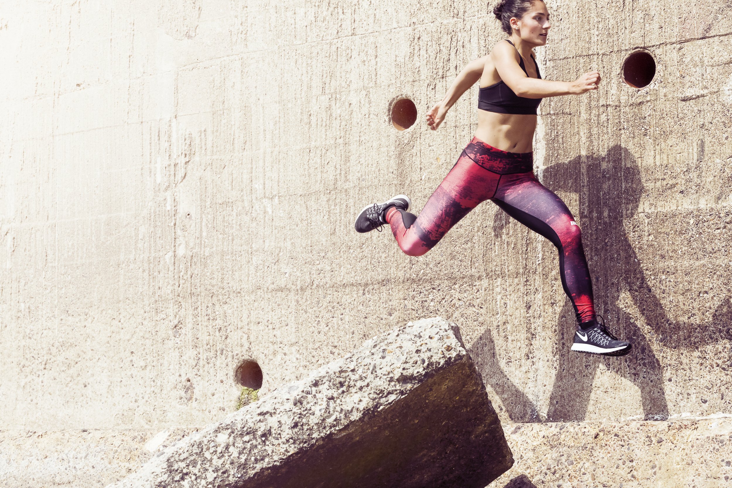 A lifestyle action shot of woman in sportswear jumping over concrete