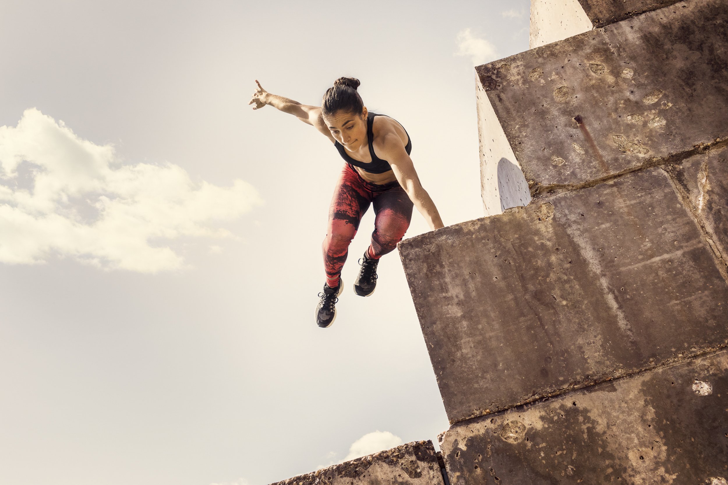 A lifestyle portrait of a woman in sportswear jumping down a wall 