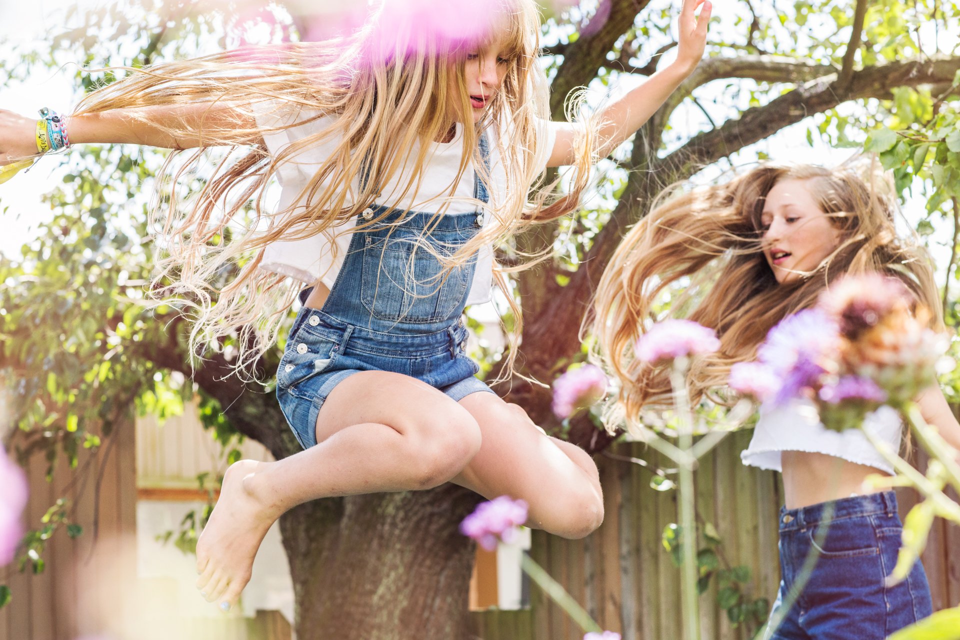 A lifestyle photo of sibling girls jumping in a garden 