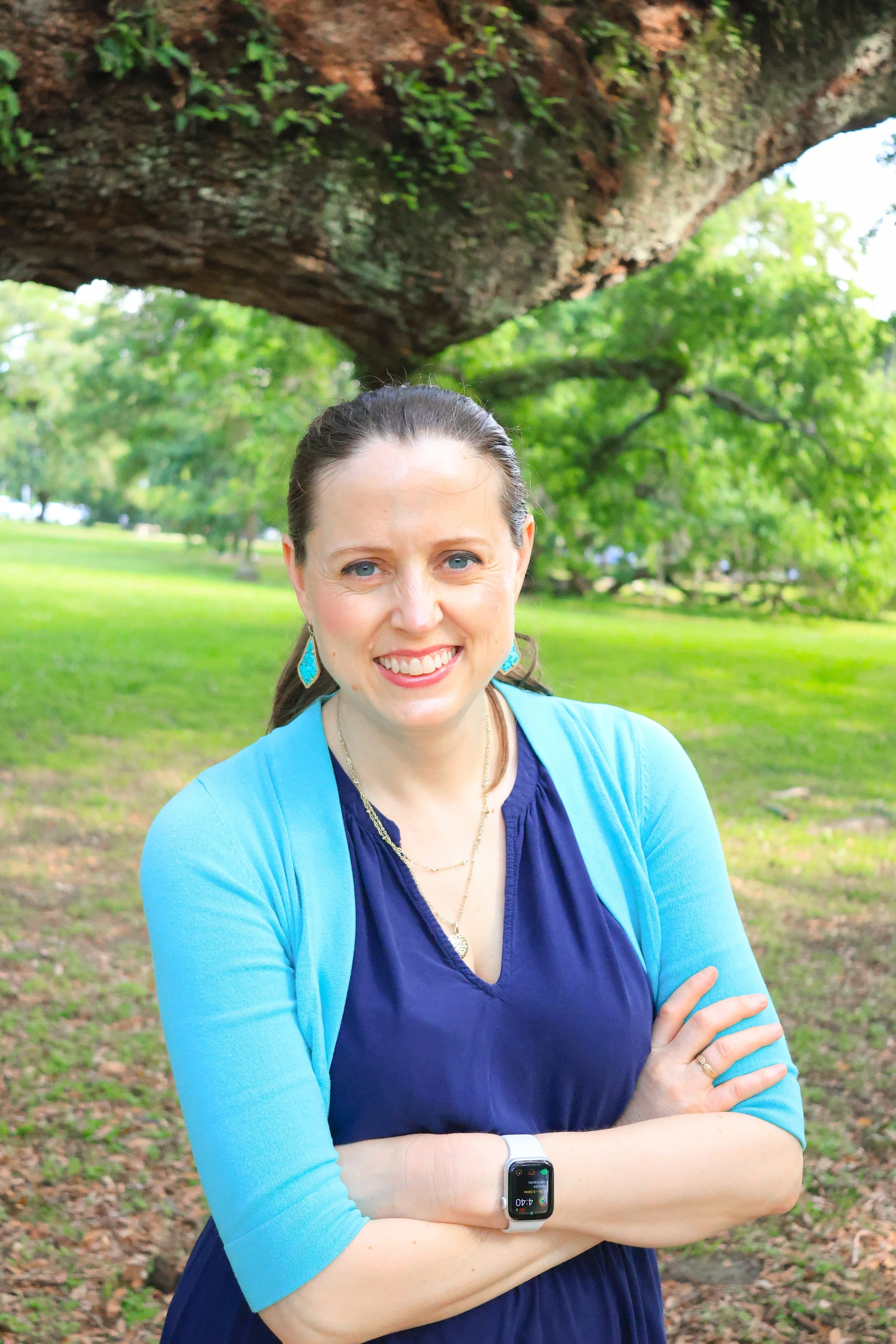 Mary Elizabeth stands smiling outside with her arms crossed in front of a tree.