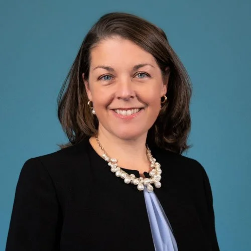 Woman with brown hair, blue jacket, grey background
