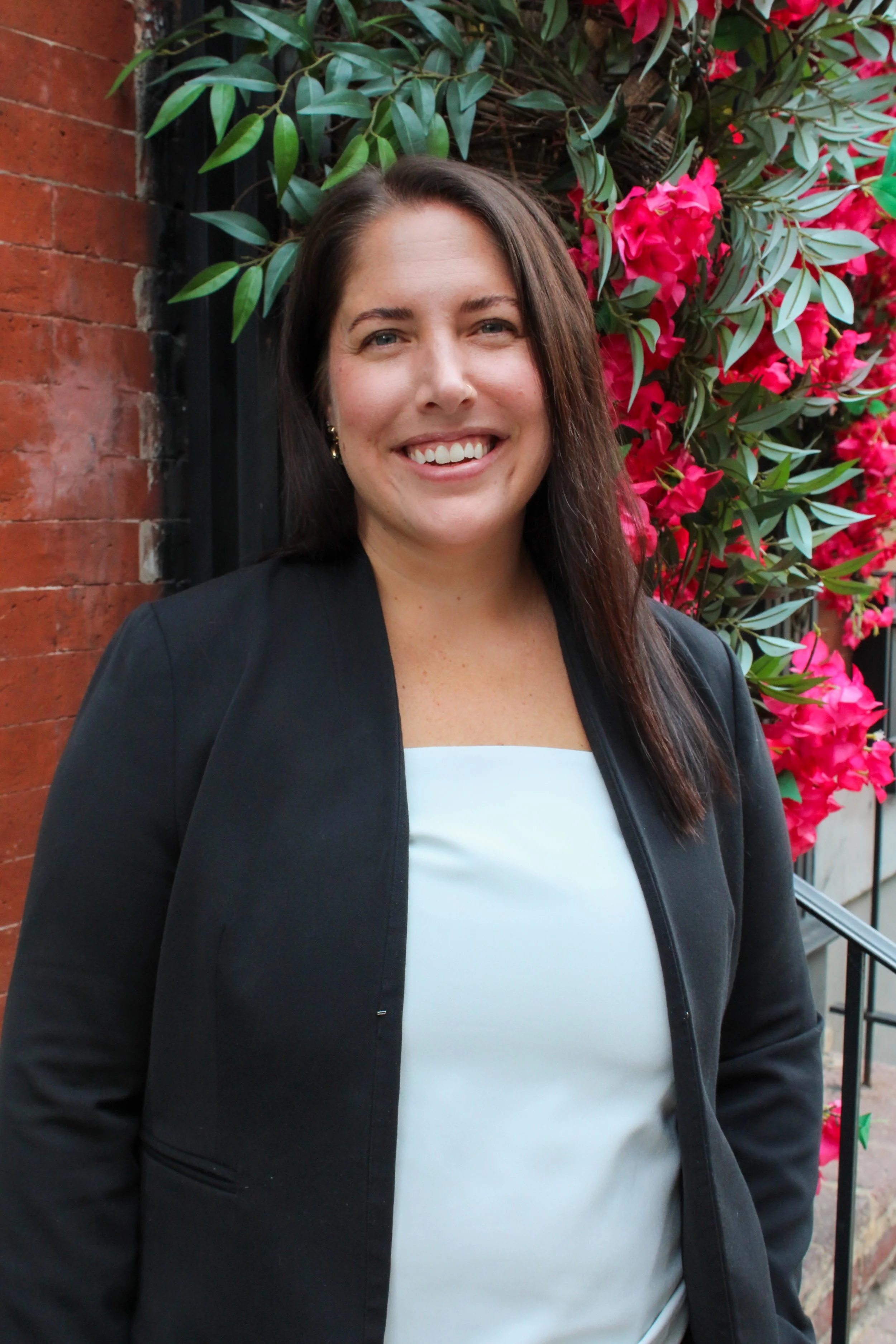 Woman with long brown hair, black blzer and flowers in the background