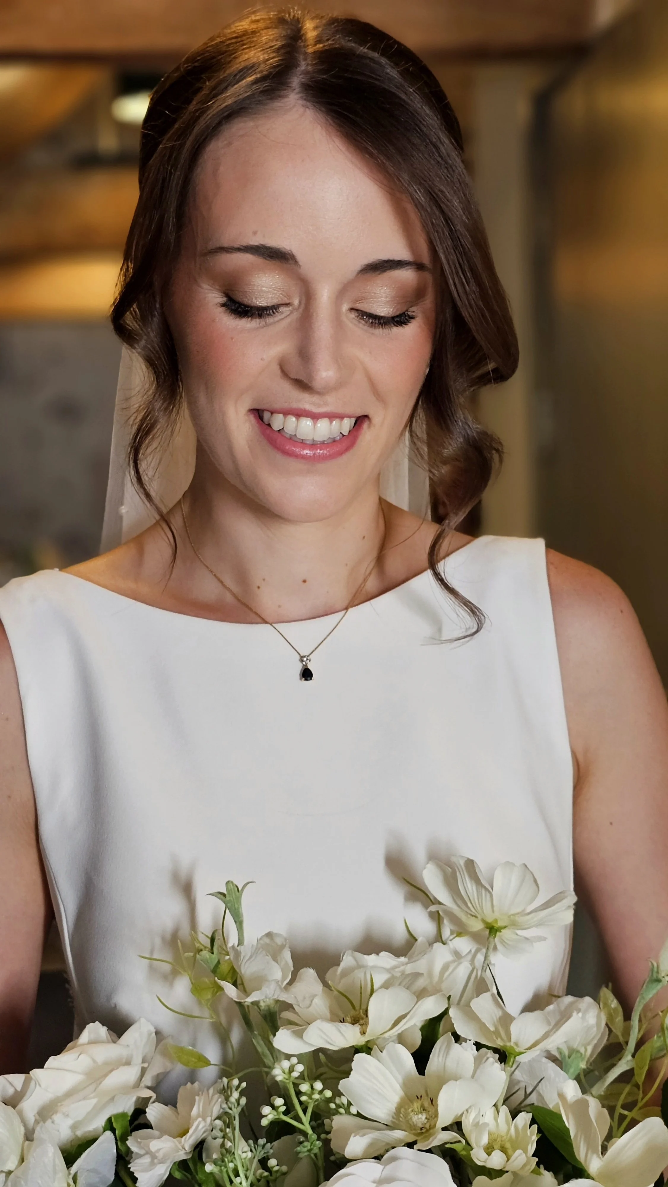 A smiling woman in a white dress holding a bouquet of white flowers, with her eyes closed.