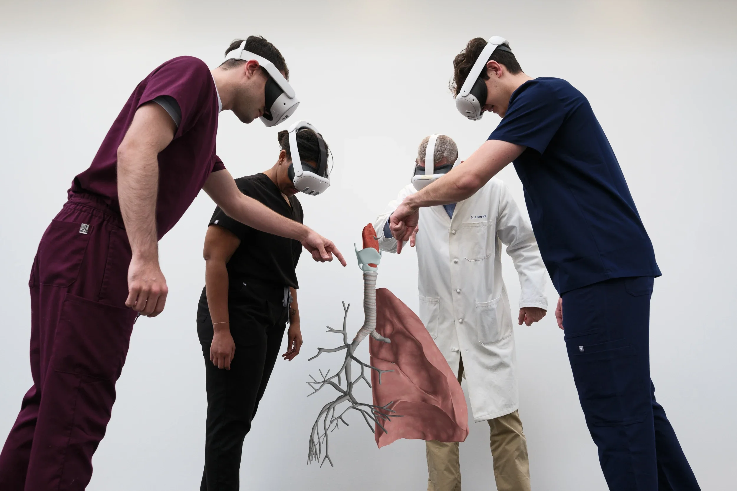 Four people, wearing virtual reality headsets, gather around a model of human lungs and heart.