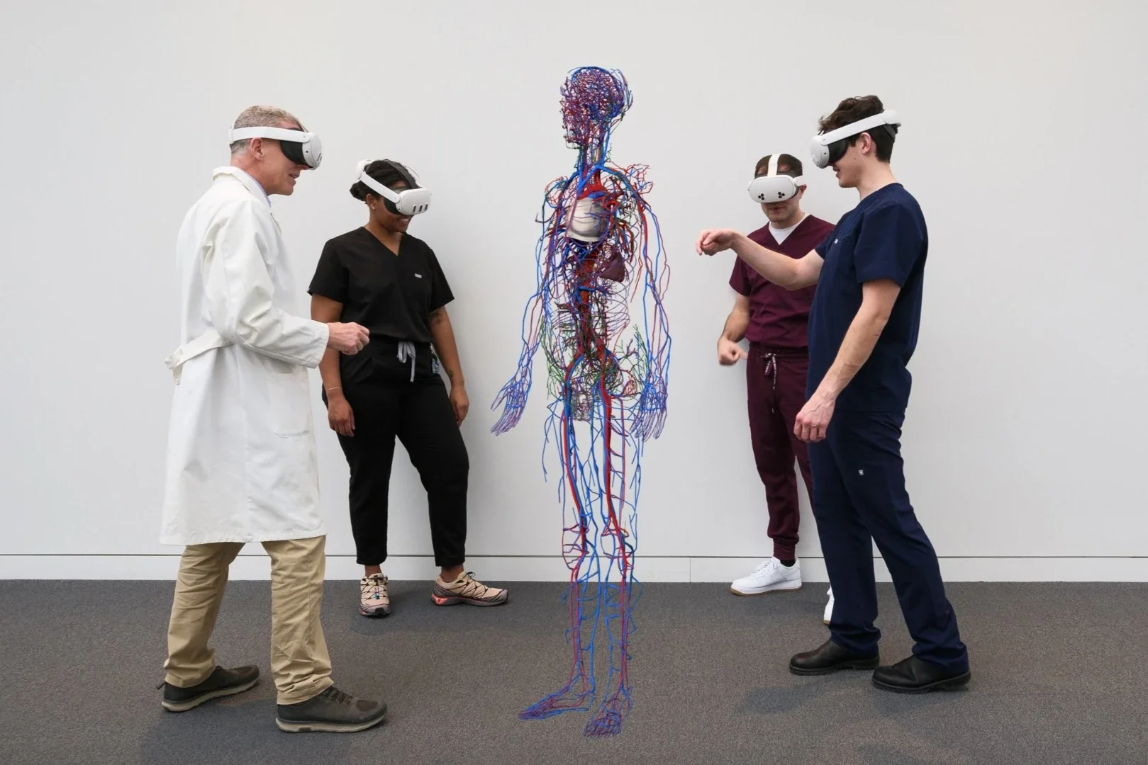 Five people in medical uniforms or scrubs wearing virtual reality goggles gathered around a 3D model of the human cardiovascular system, which is suspended in front of them.