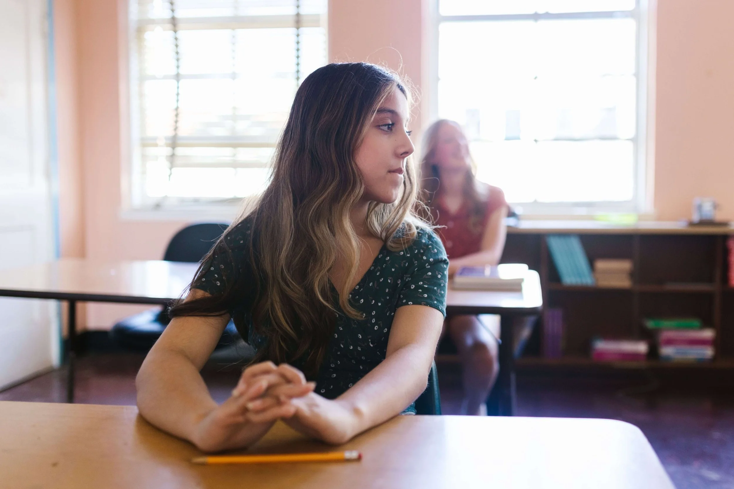 A teen girl sits at her desk in a sunlit classroom, glancing nervously to the side. What emotions come up when starting high school? Teen therapy in San Ramon, CA can help teens feel more grounded through this shift.