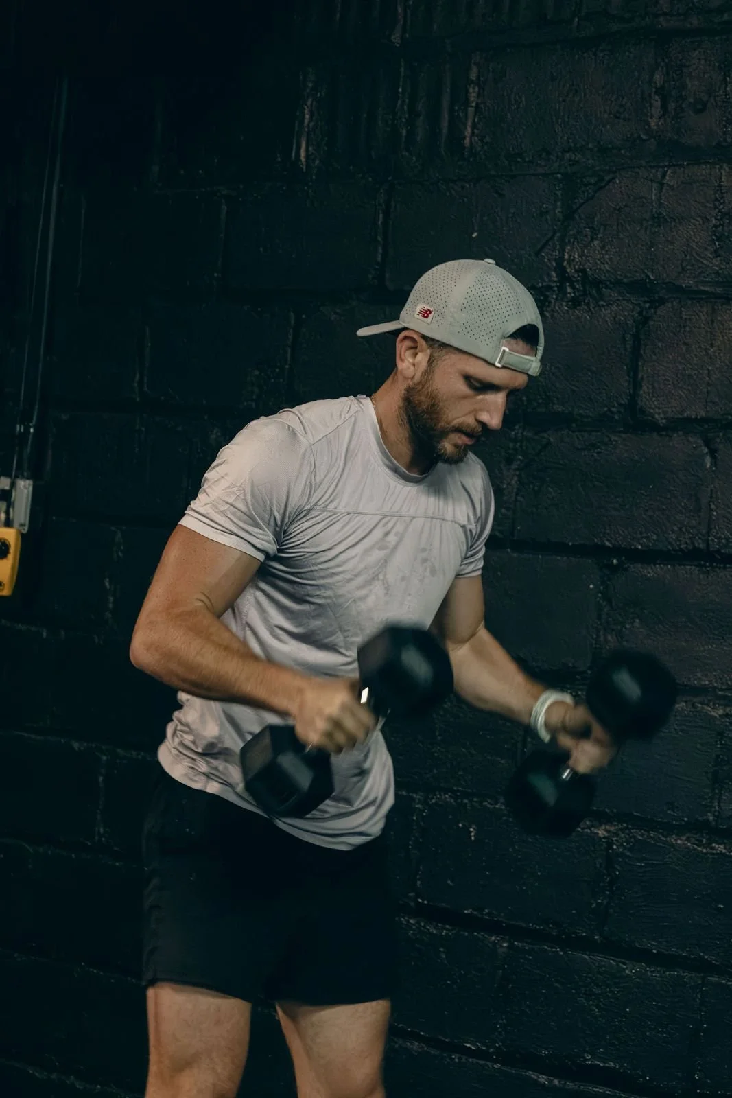 Member in a grey cap training with dumbbells against the brick wall at Char Fitness Club in Montclair, NJ