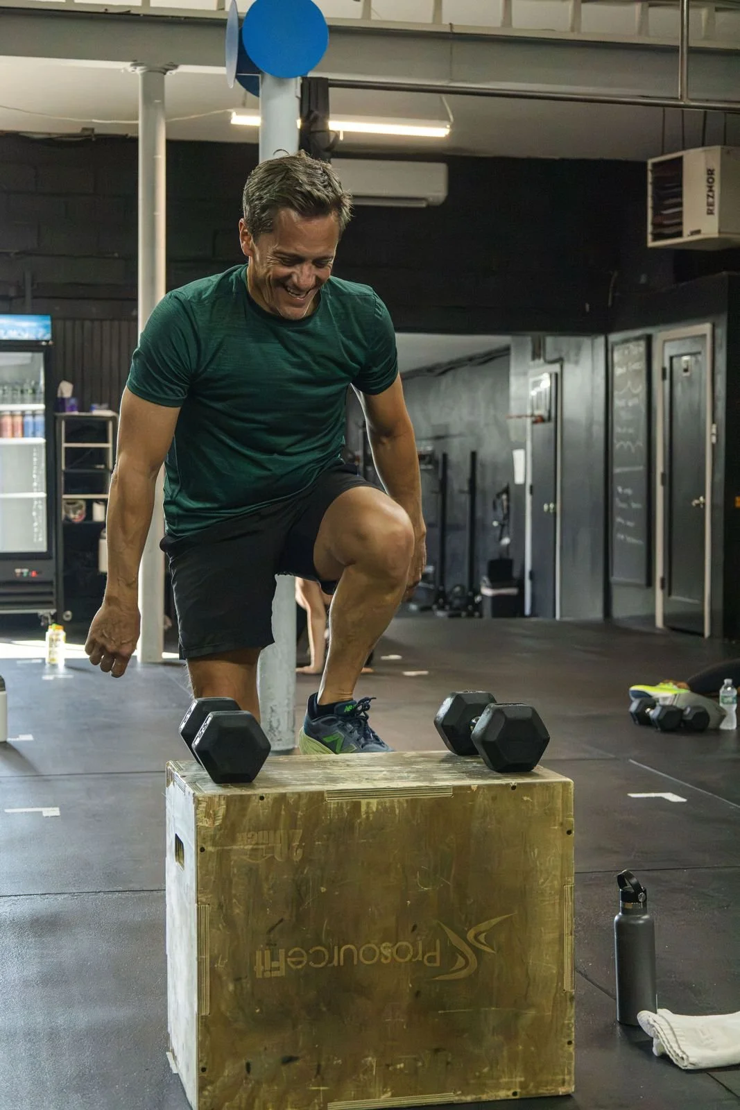 Smiling member doing a box step-up with dumbbells at Char Fitness Club in Montclair, NJ