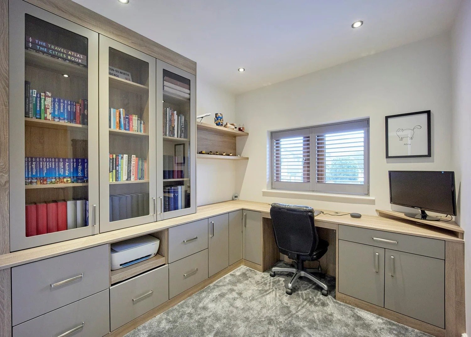Modern fitted home office with grey cabinetry, wooden worktops, glass display cabinets, and integrated desk workspace.