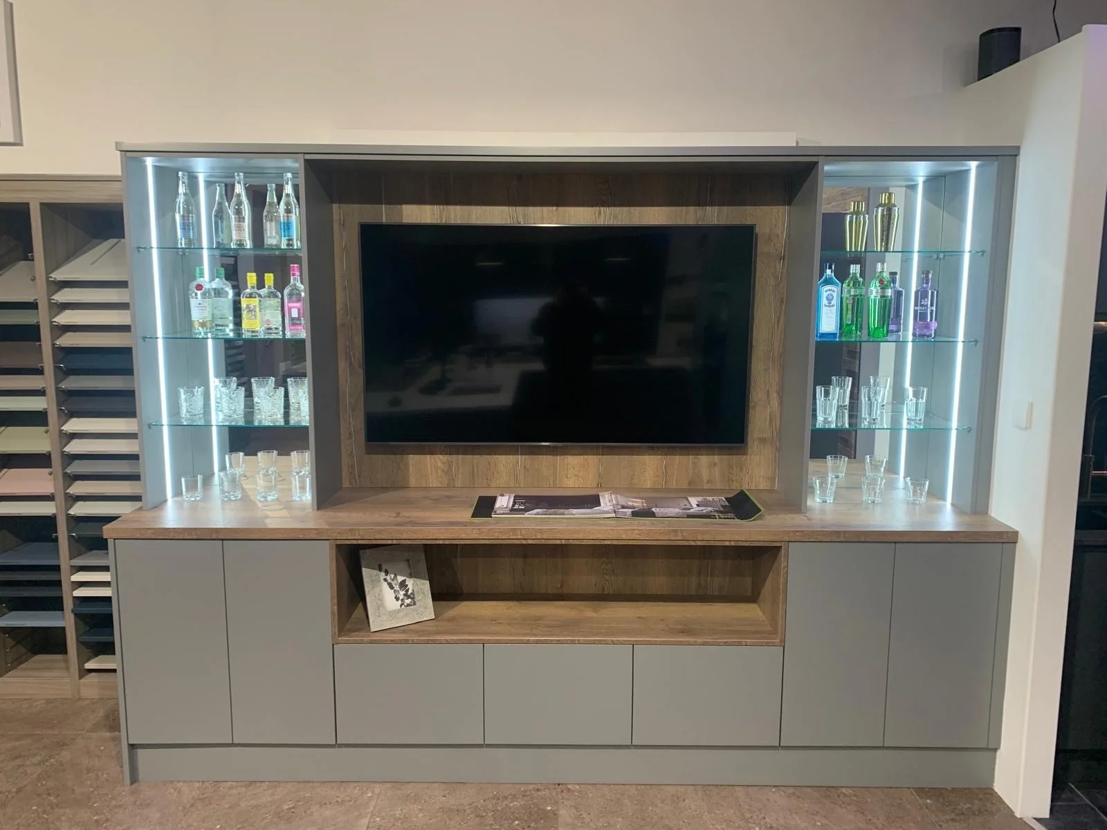 Contemporary bespoke media unit with integrated TV, illuminated glass display cabinets and wood-effect shelving by Fineline Interiors.