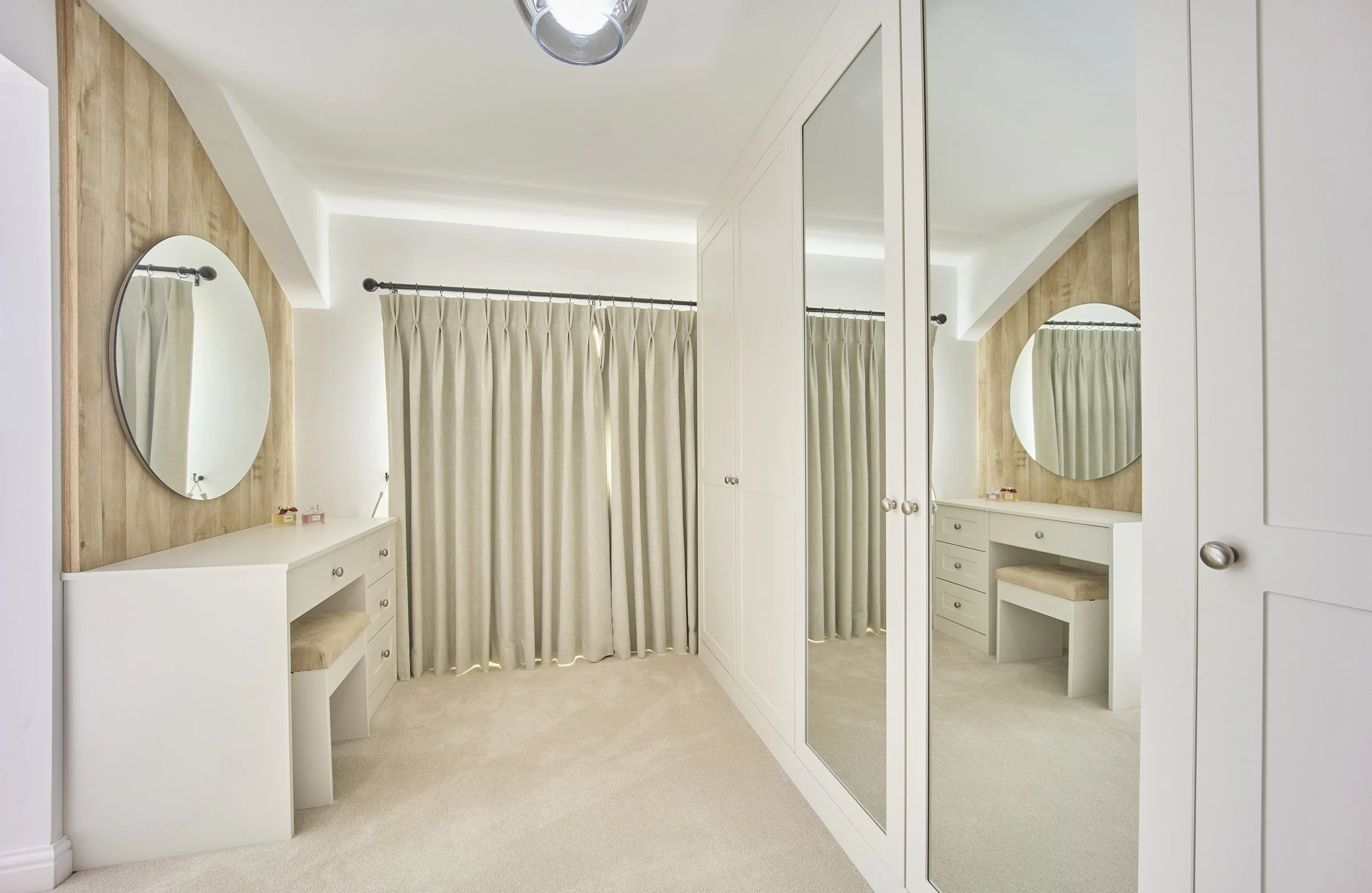 Bright bespoke dressing room with mirrored fitted wardrobes, built-in vanity unit and soft neutral finishes by Fineline Interiors.