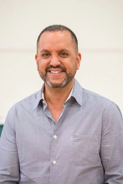 A man in a light blue button-up shirt smiling at the camera.