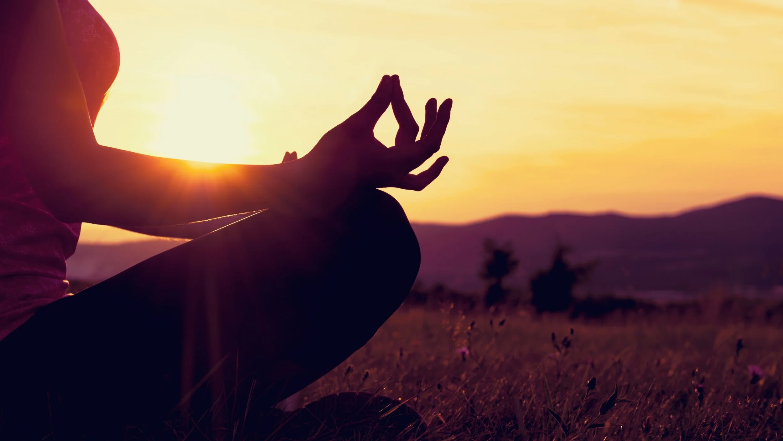 woman sitting calmly in yoga pose as sun sets
