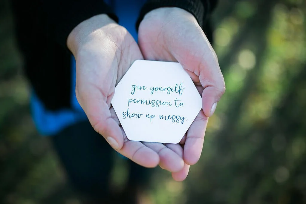 NYC anxiety therapist Maya holds a card that reads "give yourself permission to show up messy." Women with anxiety can get anxiety help in NYC here! Try online therapy for anxiety in New York too!