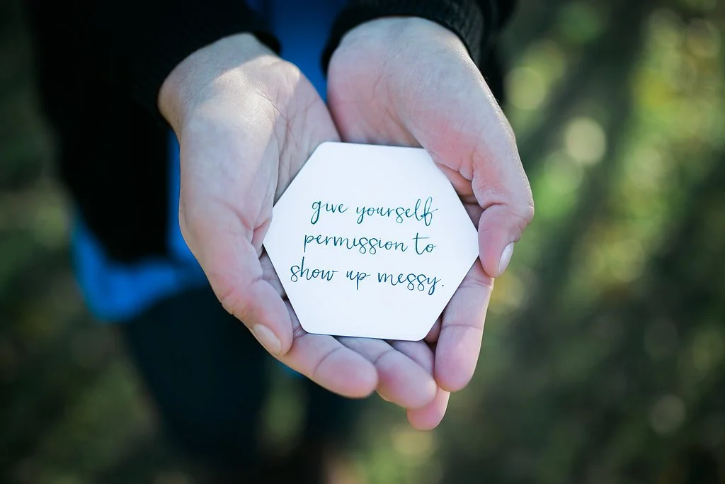 NYC anxiety therapist Maya holds a card that reads "give yourself permission to show up messy." Women with anxiety can get anxiety help in NYC here! Try online therapy for anxiety in New York too!