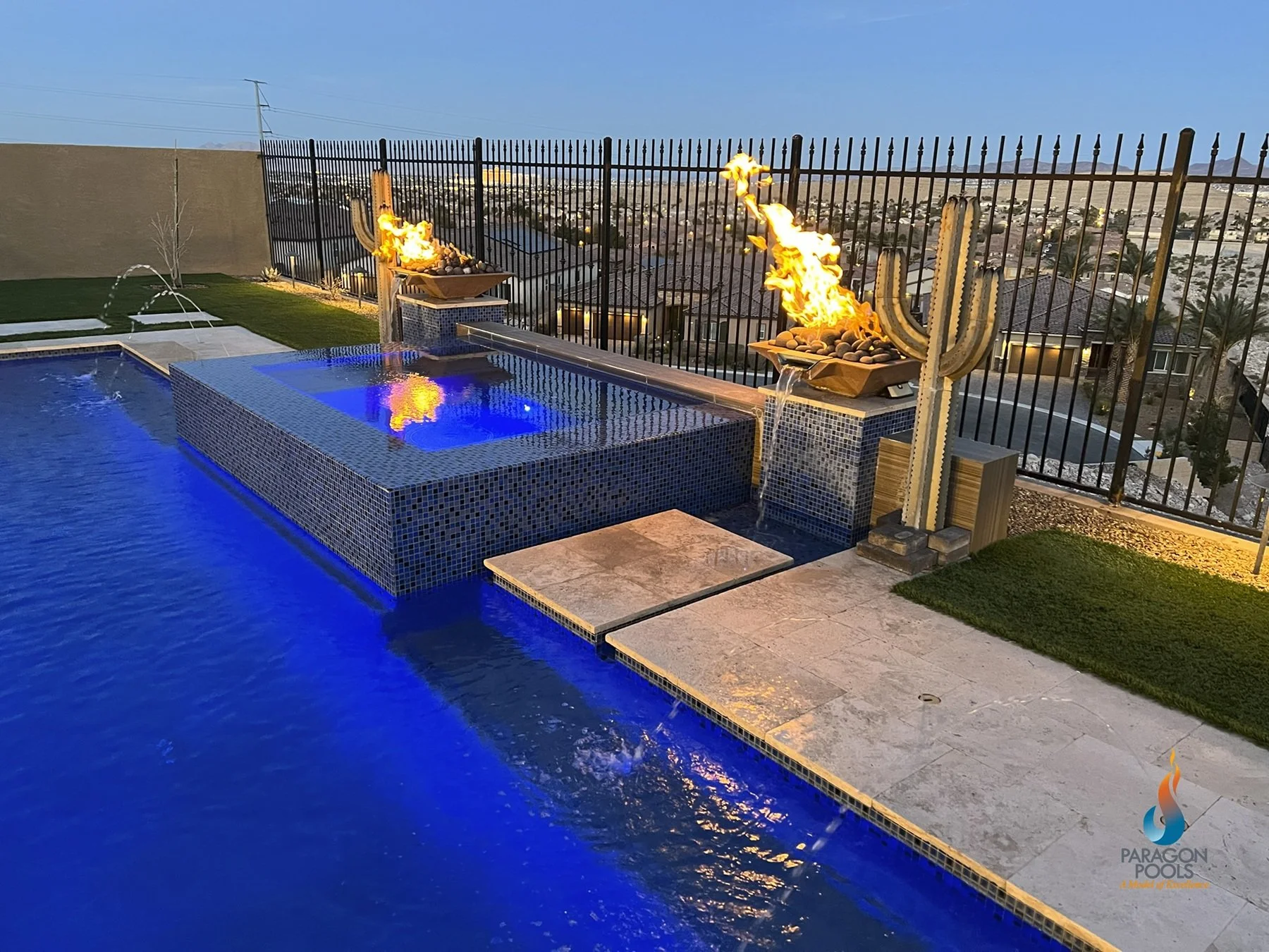 A backyard with a swimming pool featuring deck jets, a custom spa with LED lighting, and 2 combo fire and water features, custom pool by Paragon Pools.