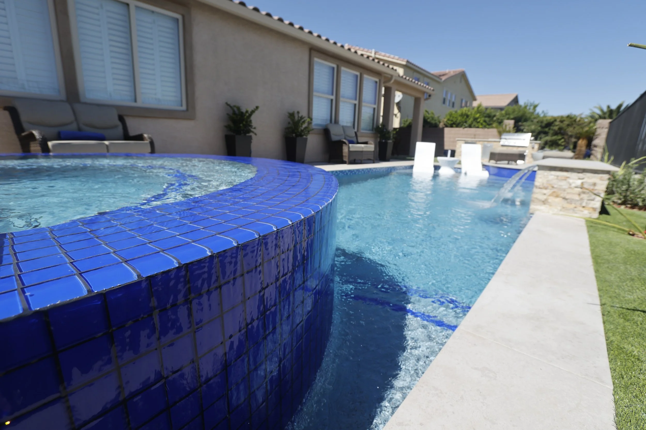 Raised spa with blue tiled spillway flowing into a pool with a tanning ledge and sheer descents