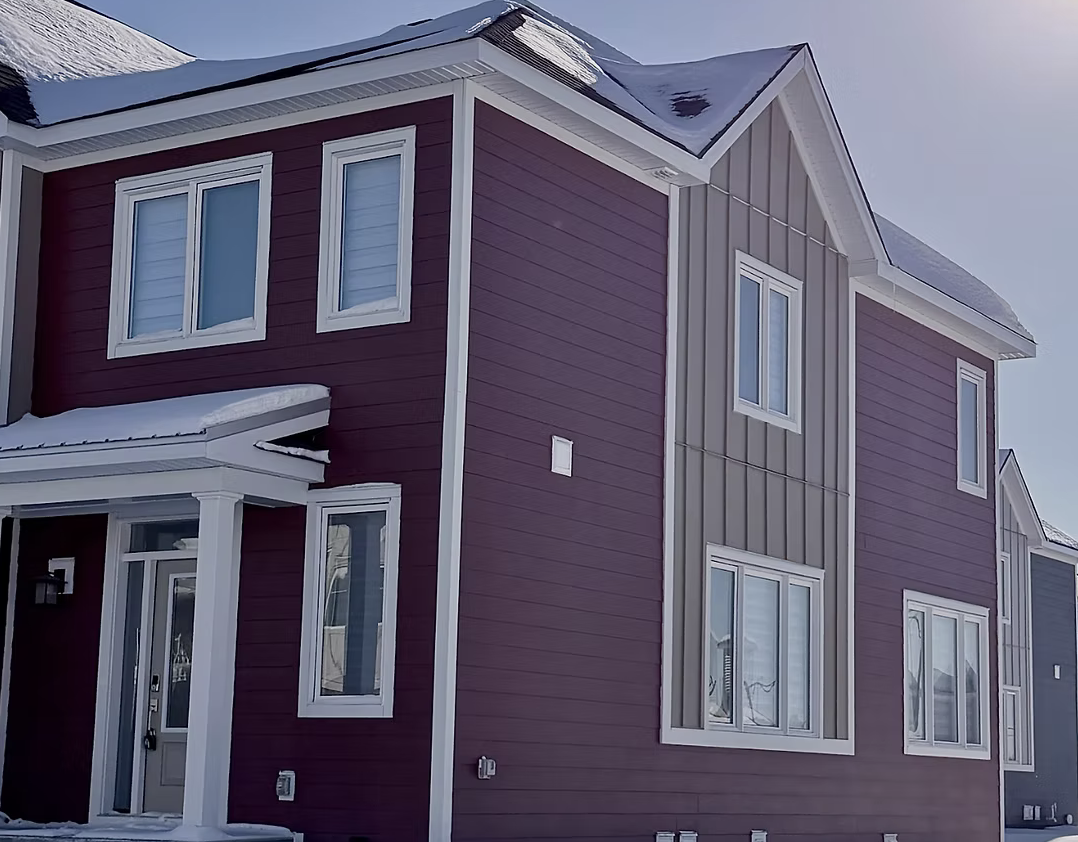 A modern, multi-story house with purple and gray siding, white trim, and snow on the roof, set against a clear sky.