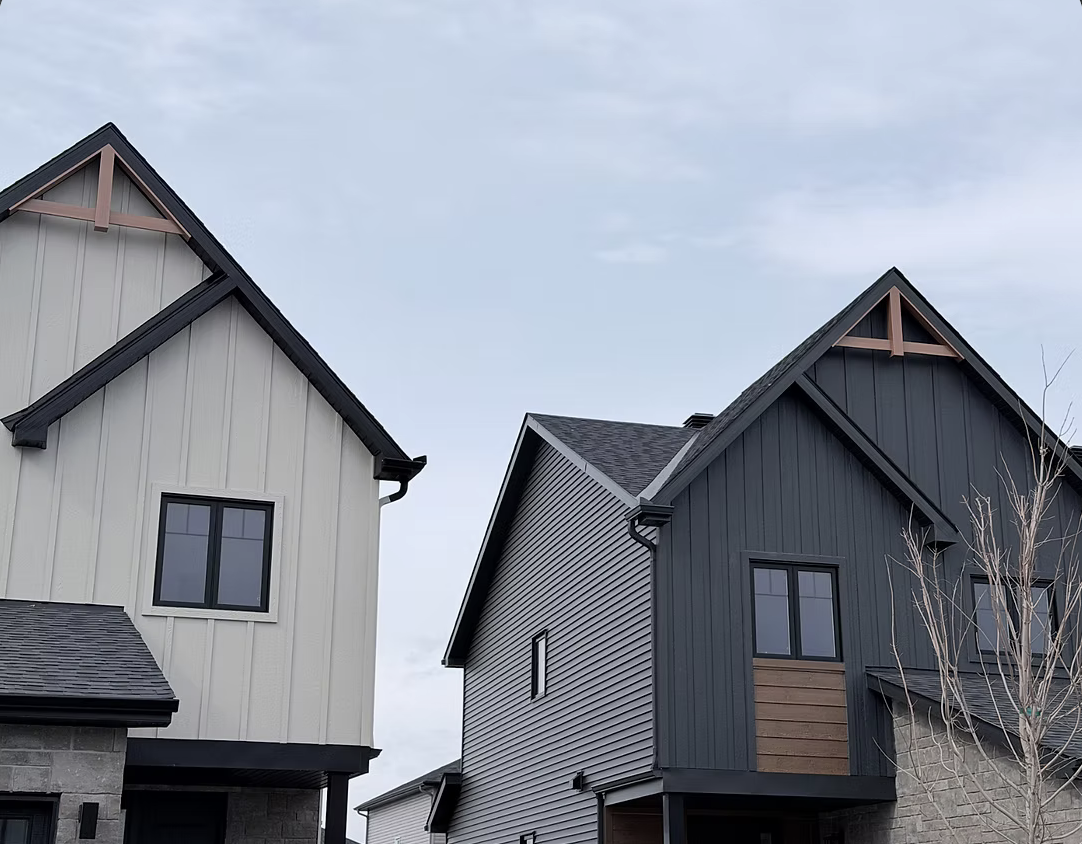 Two modern houses with sloped roofs, one with light-colored siding and the other dark-colored, under a cloudy sky.