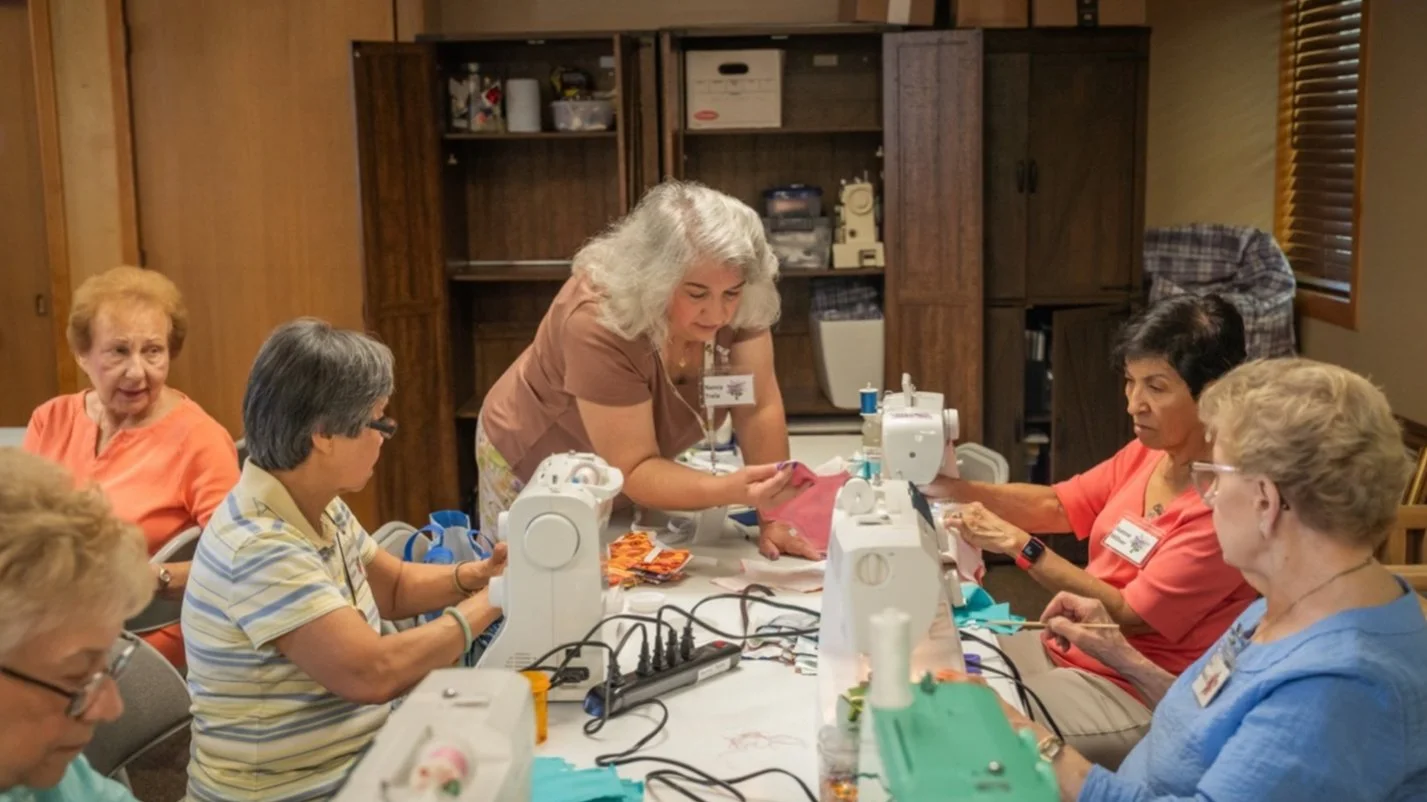 A group of women gathered around a table with sewing machines, participating in a sewing workshop to make reusable menstrual kits.
