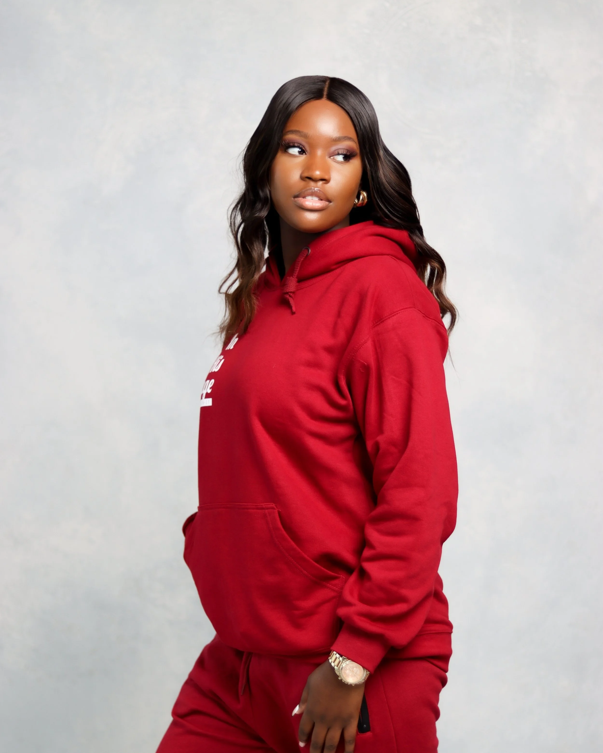 A woman with long black hair wearing a red hoodie and matching red sweatpants, standing against a plain background.