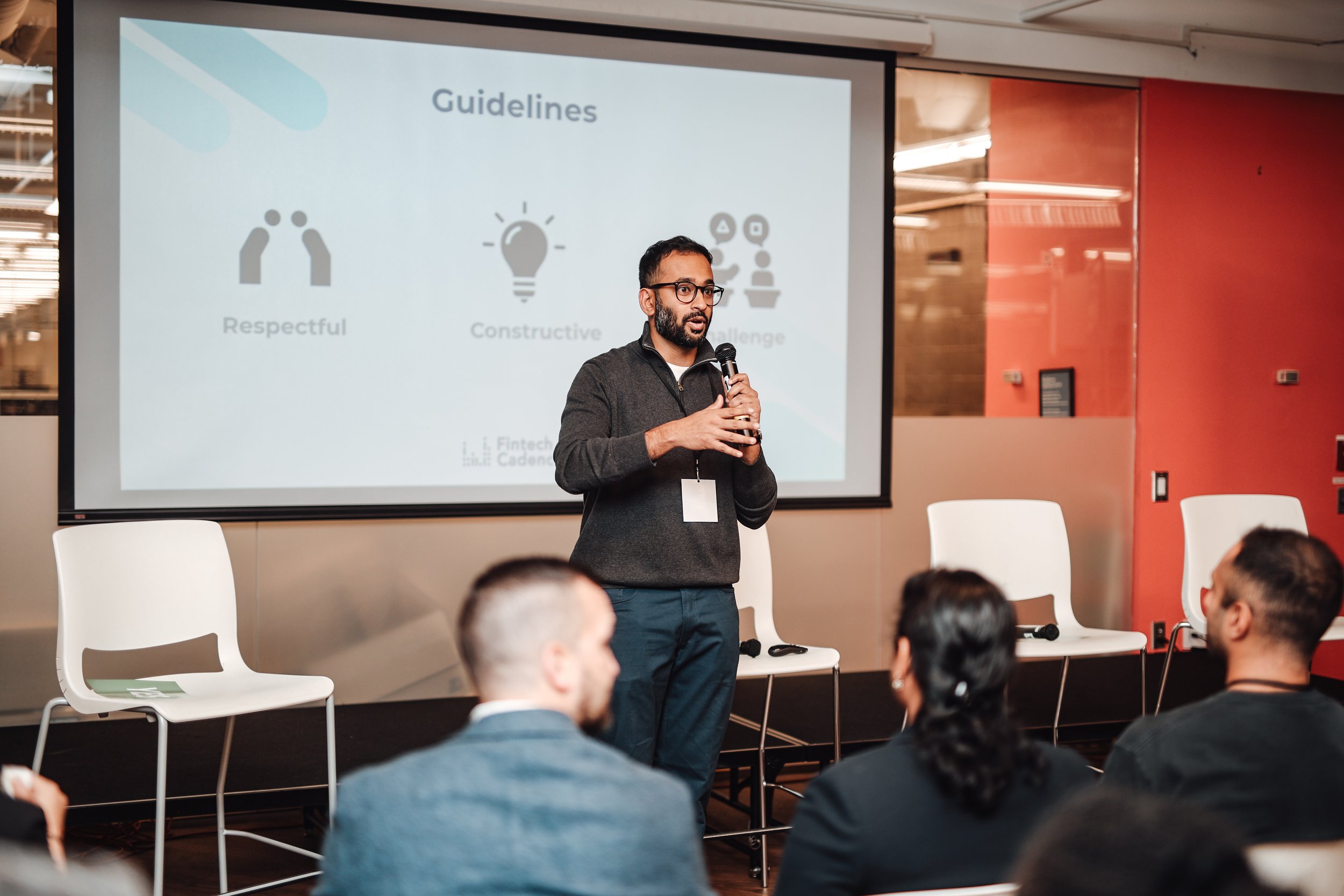 Man giving a presentation in front of an audience, standing in front of a screen displaying guidelines: Respectful, Constructive, Challenge, in a conference room.