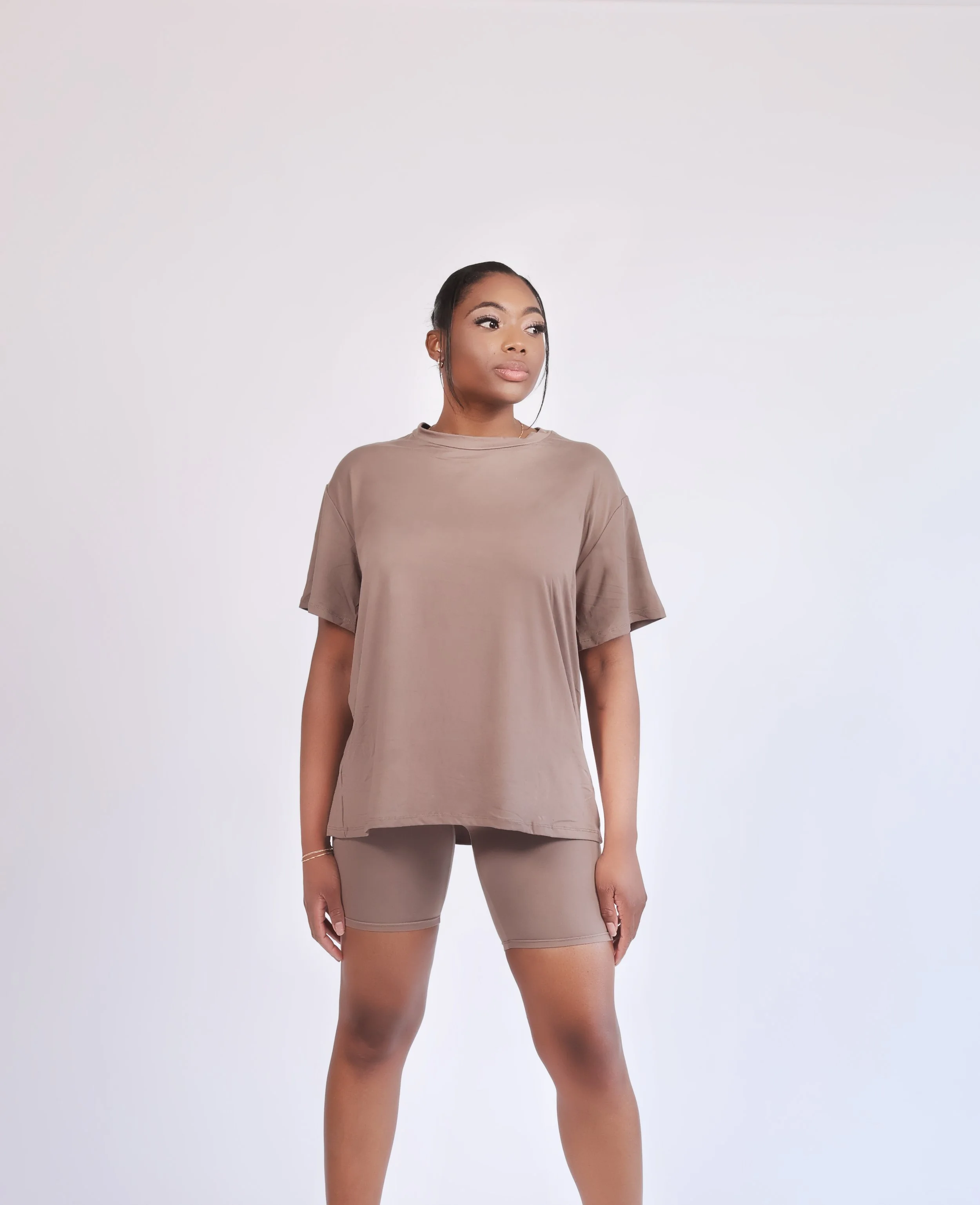 A woman wearing a loose beige T-shirt and matching beige shorts standing against a plain white background.