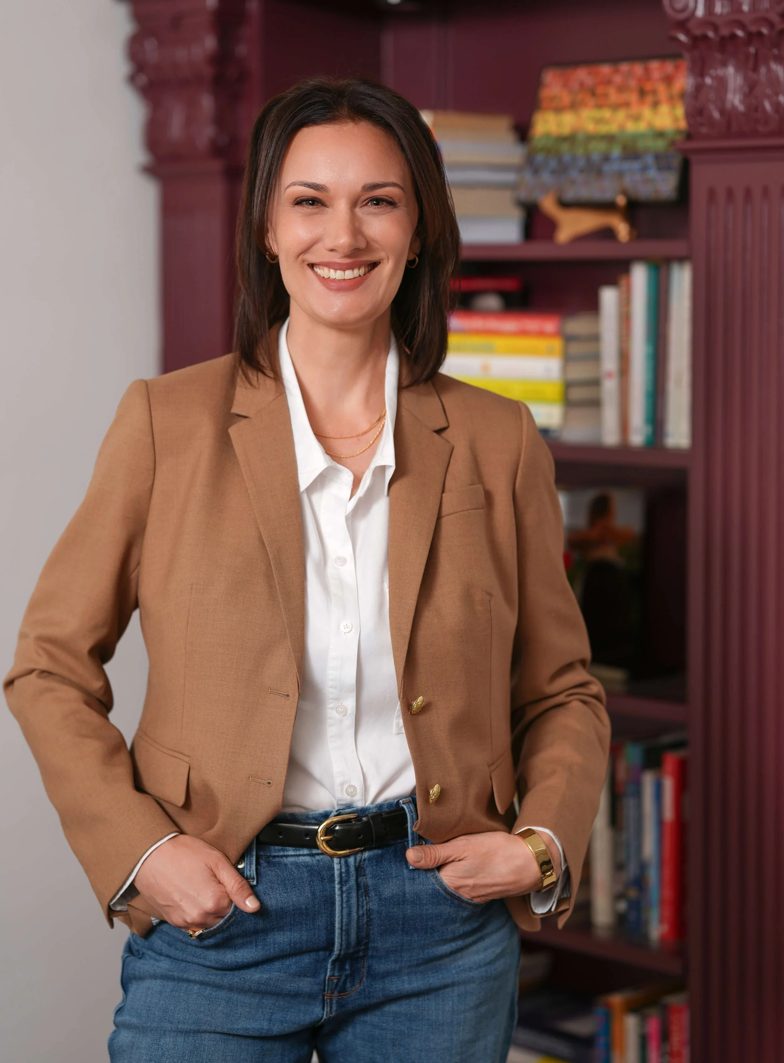 Sara Havlik, LMSW in a tan blazer and white shirt standing in front of her office bookshelf