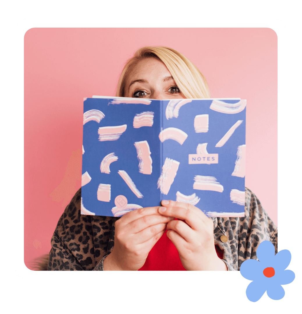 Kate - studio owner of Kurly Creative playfully hiding behind a colorful blue patterned note book