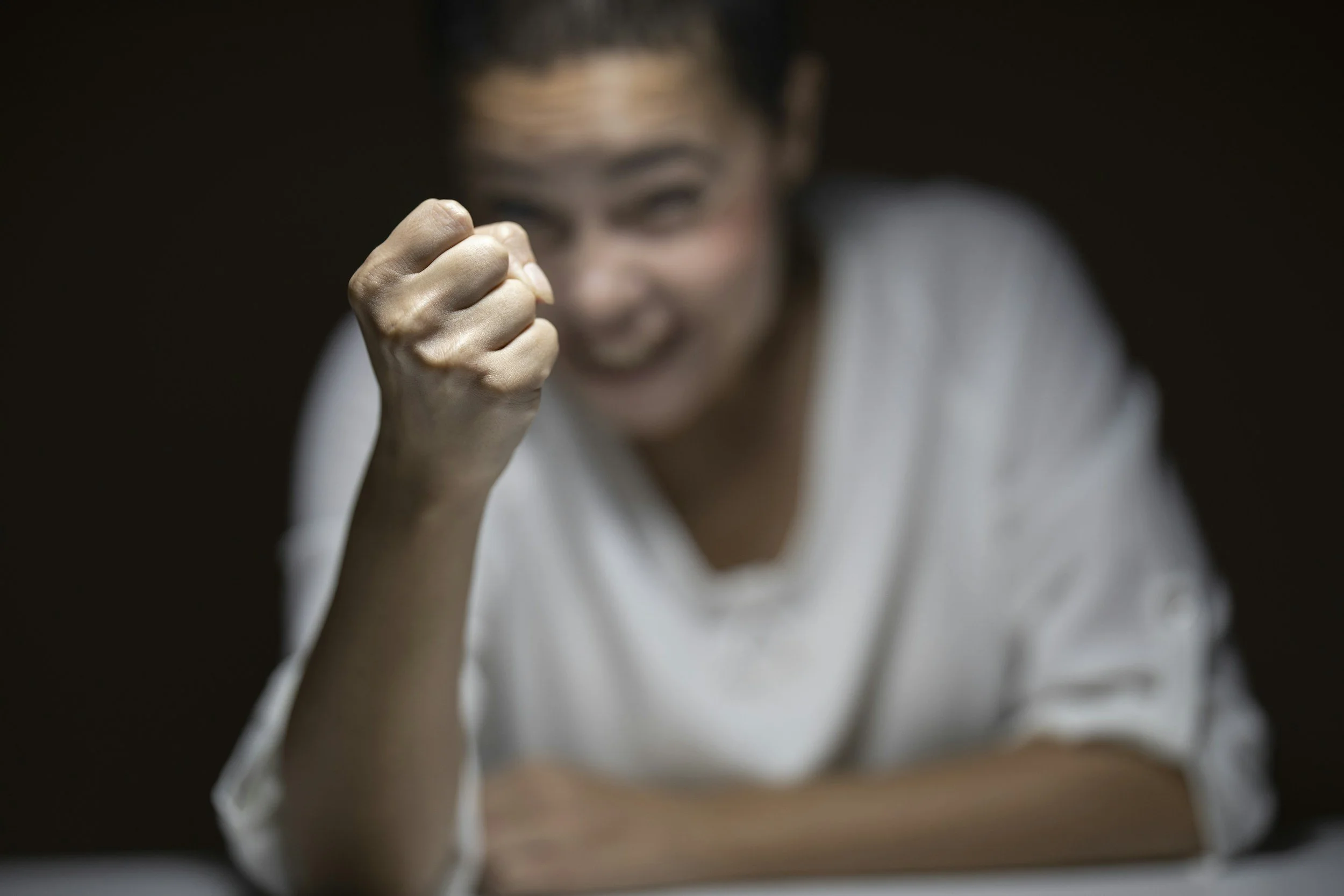Woman smiling with fist raised in a gesture of triumph or determination, blurred background.