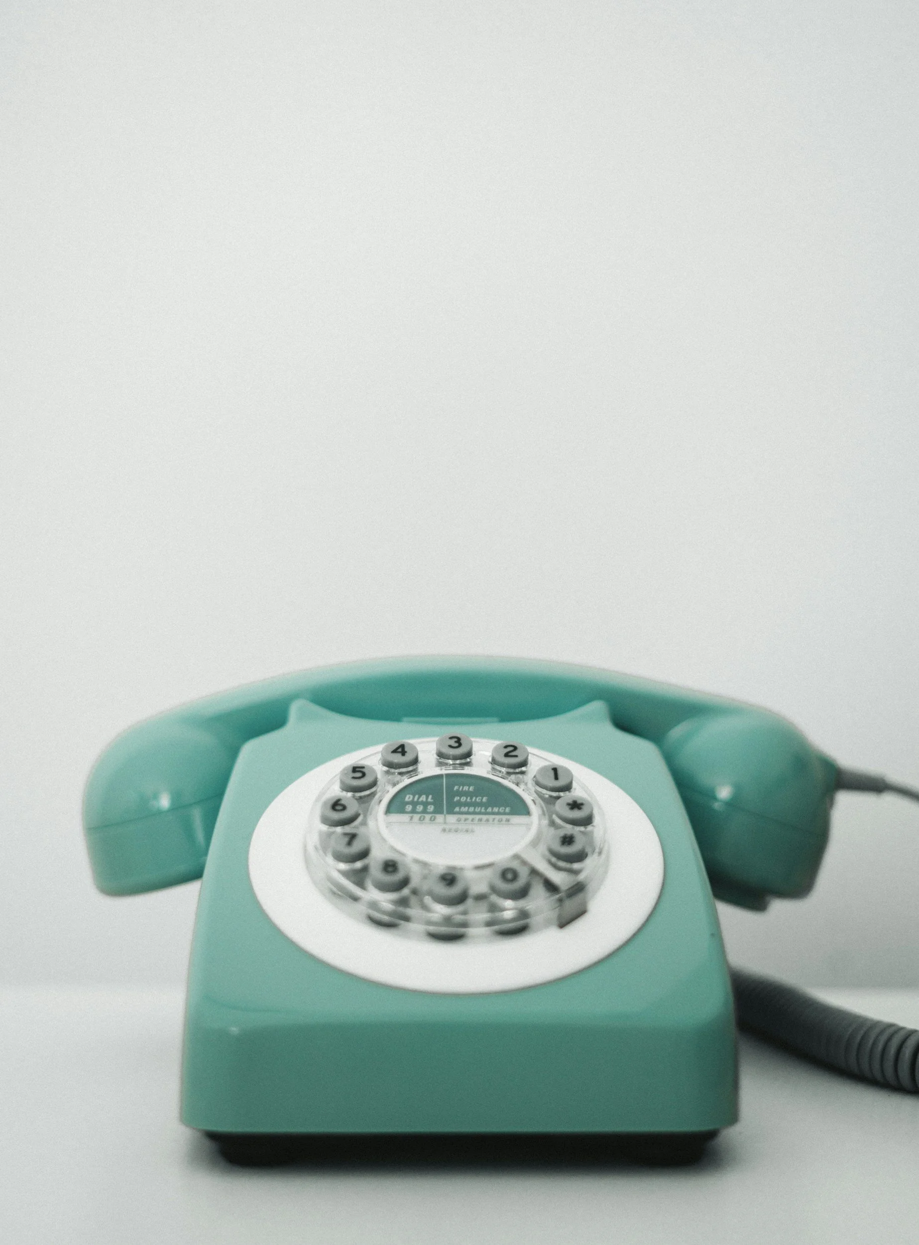 Vintage teal rotary telephone with a coiled cord on a plain white surface.