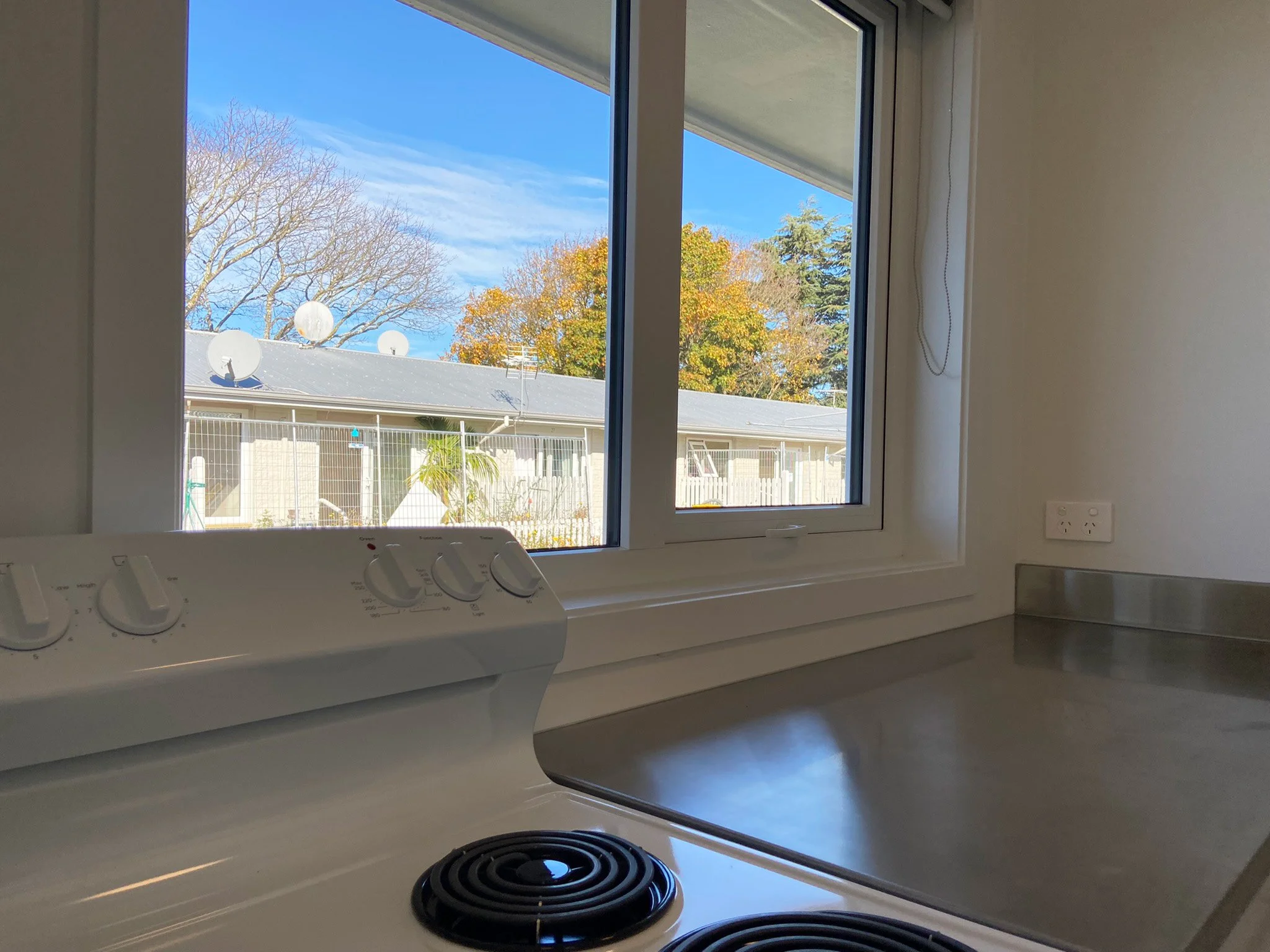 View of kitchen stove and countertop with other OCHT visible homes through window