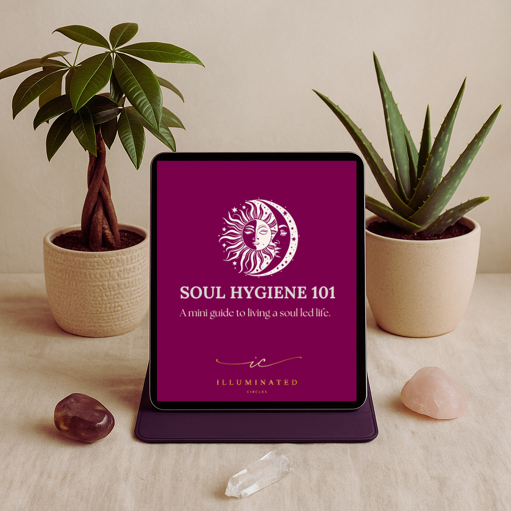 A digital tablet displaying the cover of 'Soul Hygiene 101: A mini guide to living a soul led life' with mystical sun and moon face artwork, placed on a beige table surrounded by two potted plants, a brown stone, a pink stone, and a clear crystal.