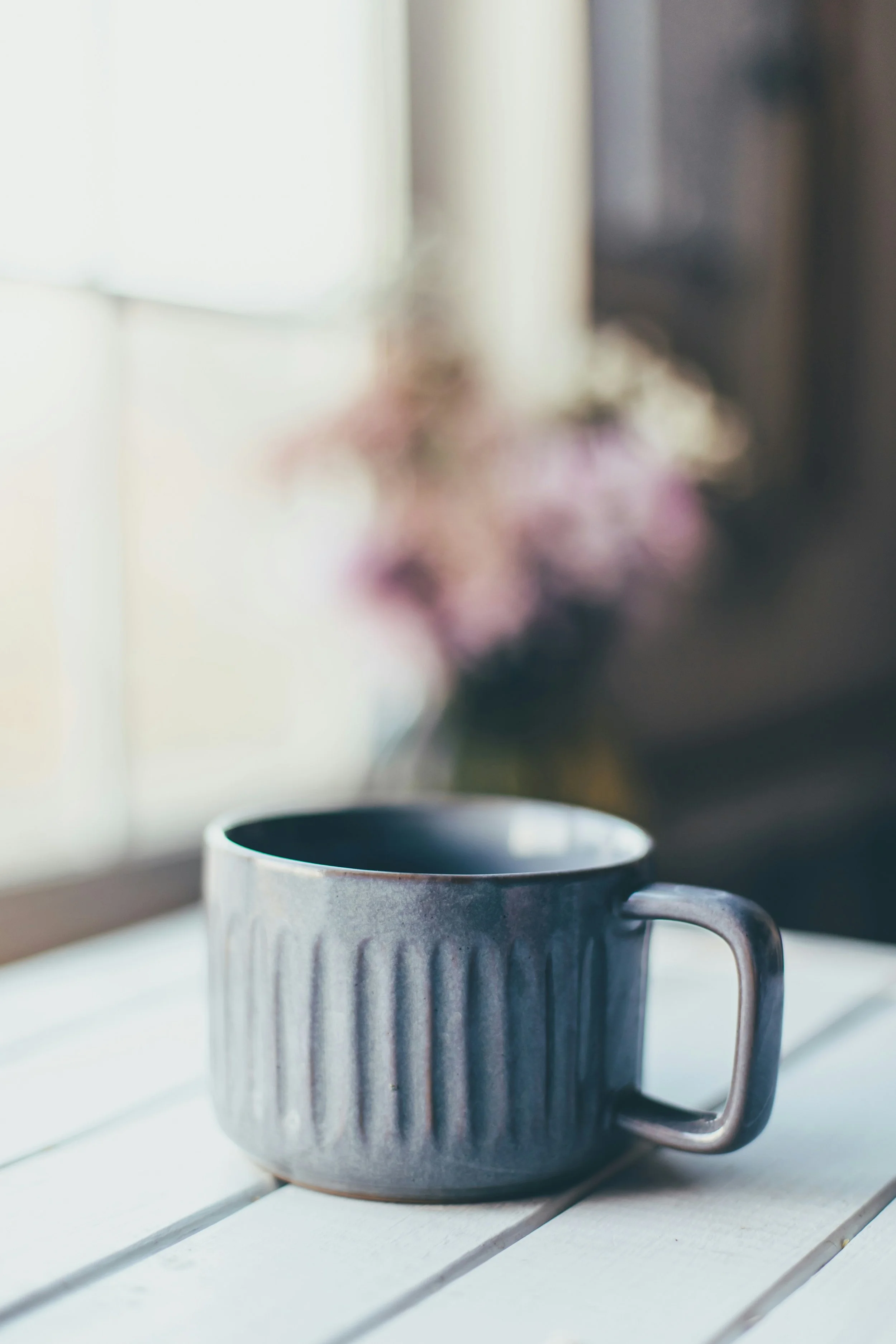 Gray, ceramic mug on a table in front of flowers and a window | Individual therapy with a couples therapist in NC, OH, VA, and WV