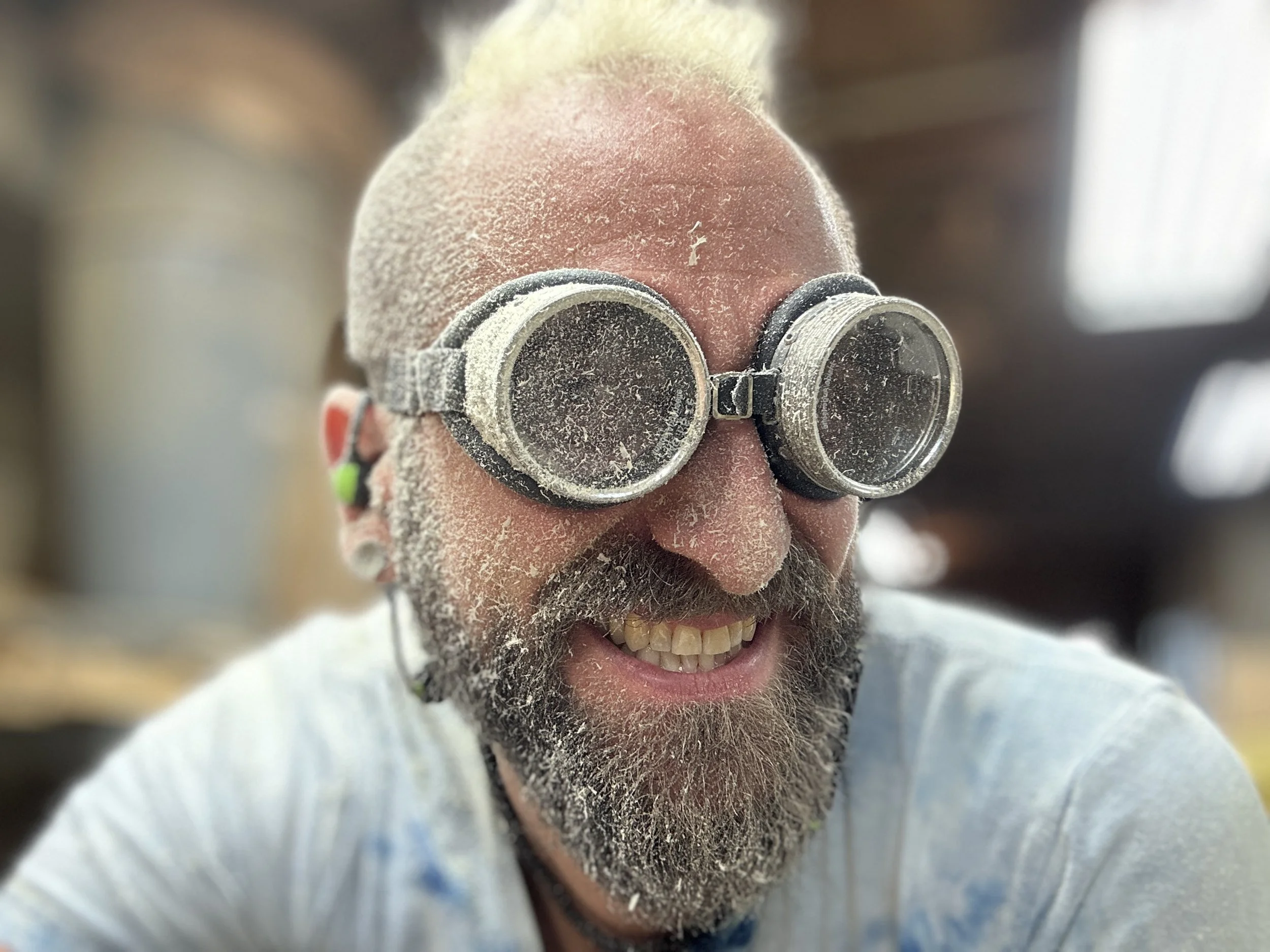 Greg Westby, Founder of Mount Westby Made custom luxury furniture and cabinetry, wearing goggles, smiling wide, covered in sawdust.