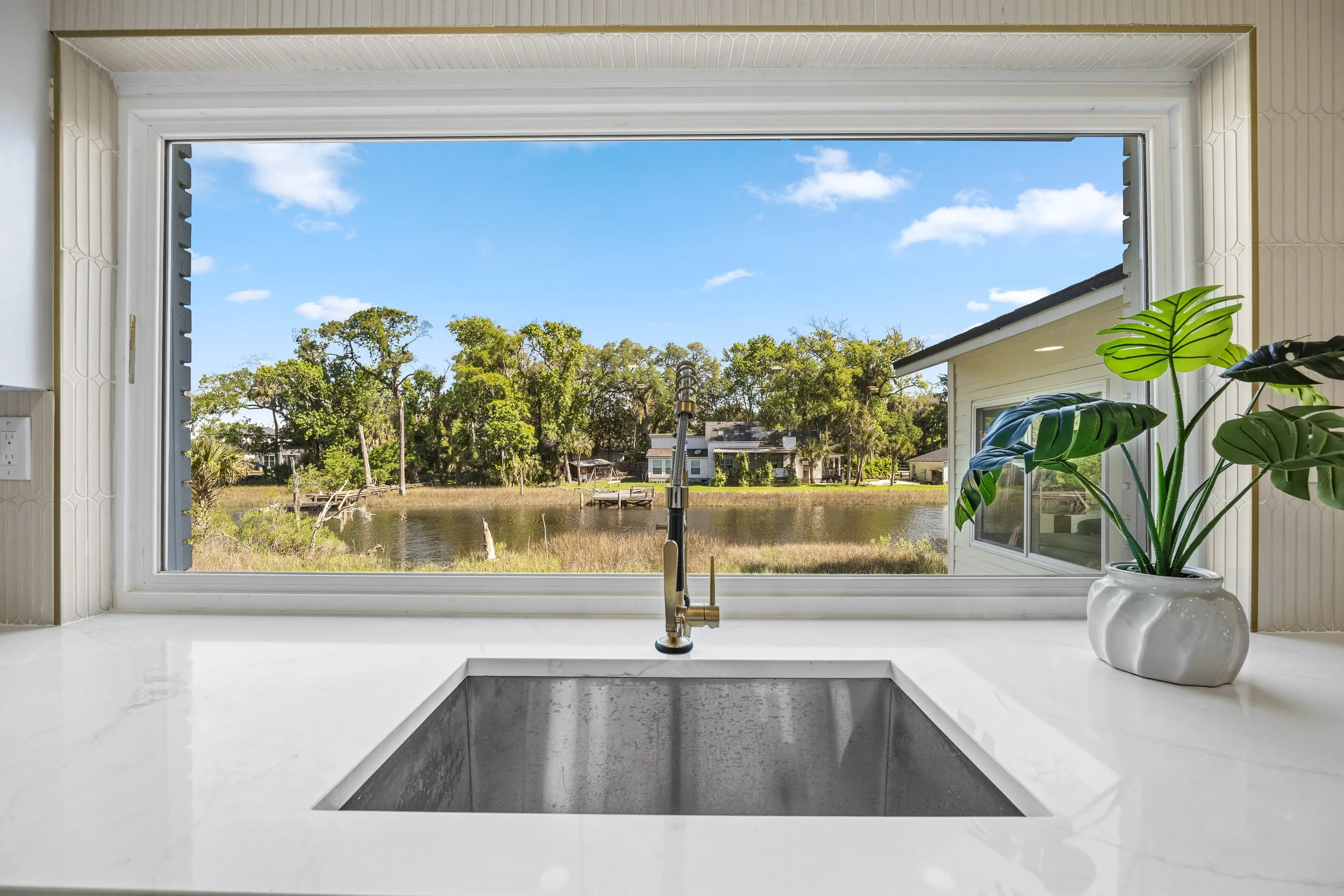 Kitchen sink beneath a picture window overlooking a marsh pond and native landscaping.