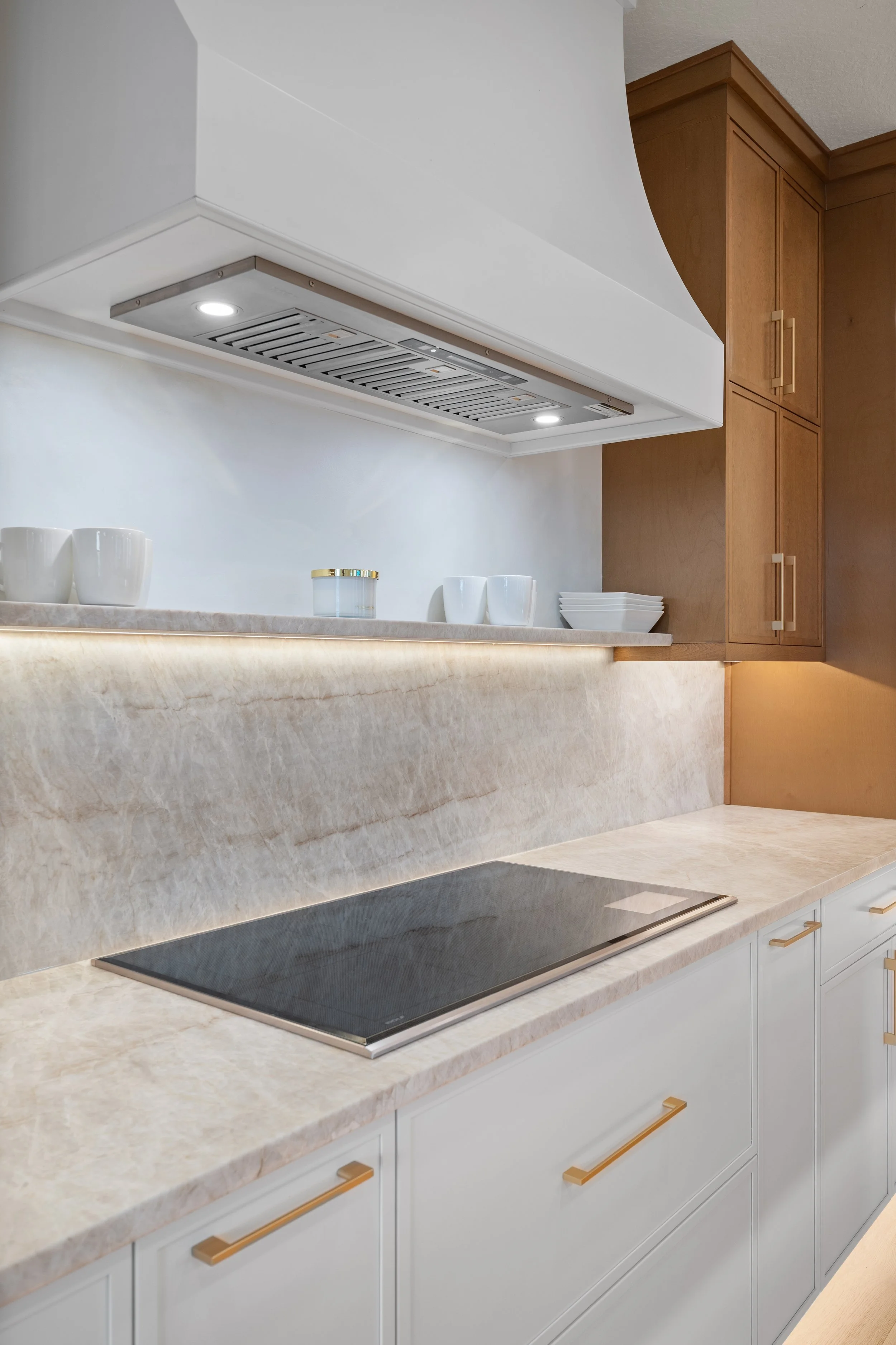 Modern kitchen with white cabinetry, marble countertop, black cooktop, and upper wooden cabinets.