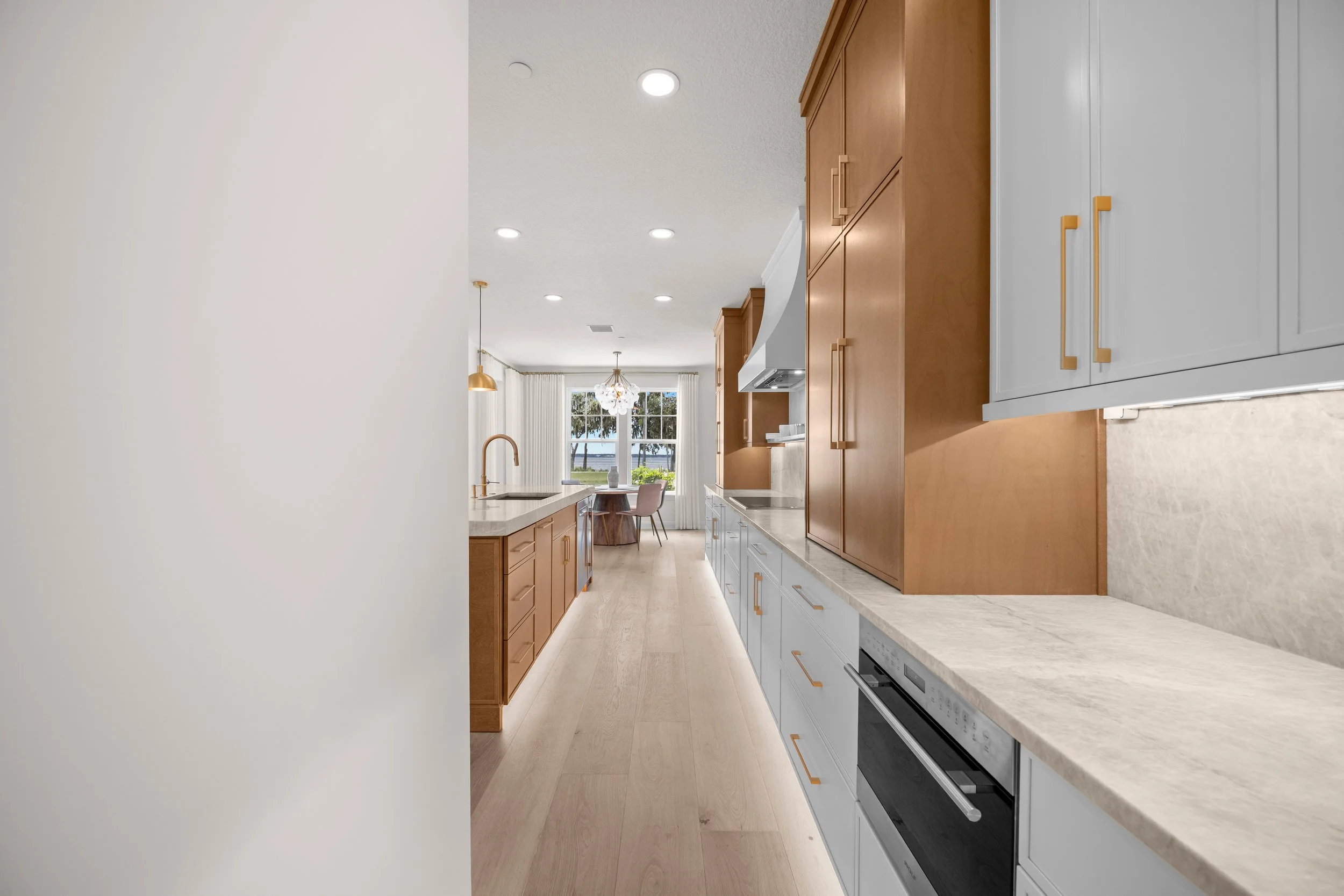 Modern kitchen with white and wood cabinetry, marble countertops, and large window with curtains, bright and airy.