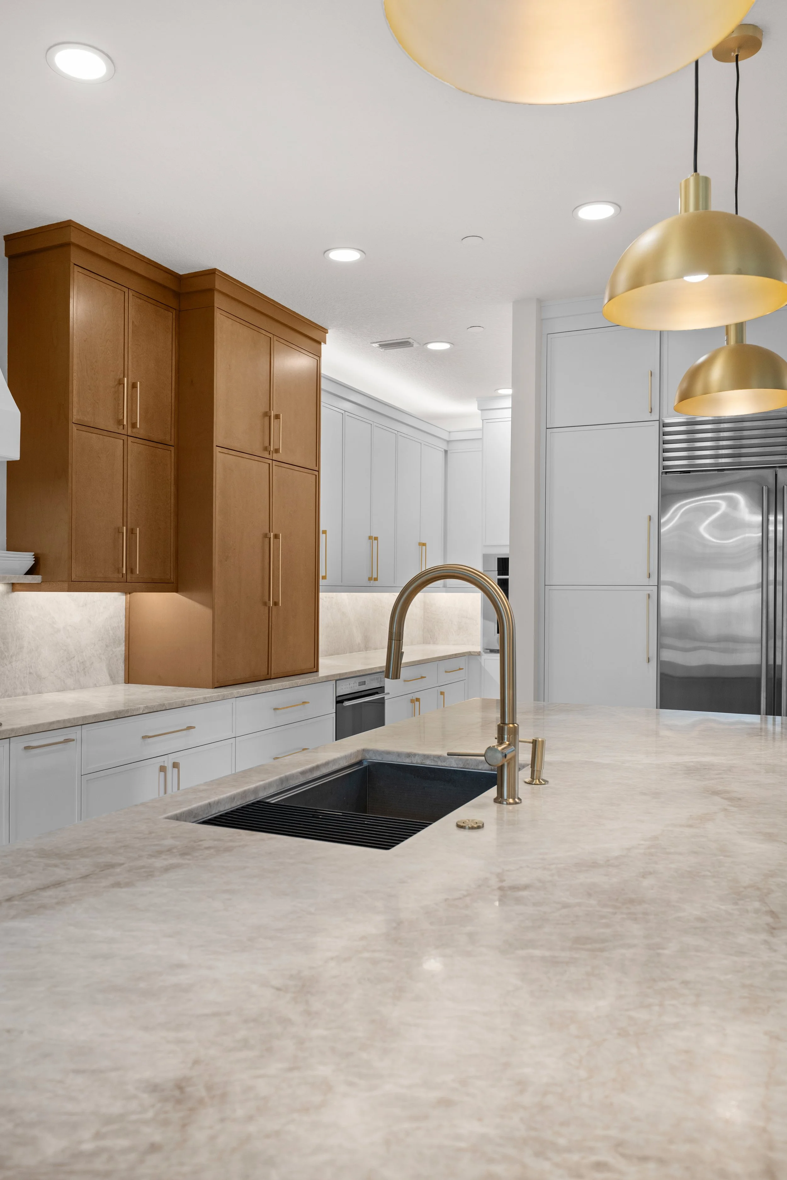 Modern kitchen with white and wooden cabinets, gold pendant lights, a black sink, and a marble countertop.