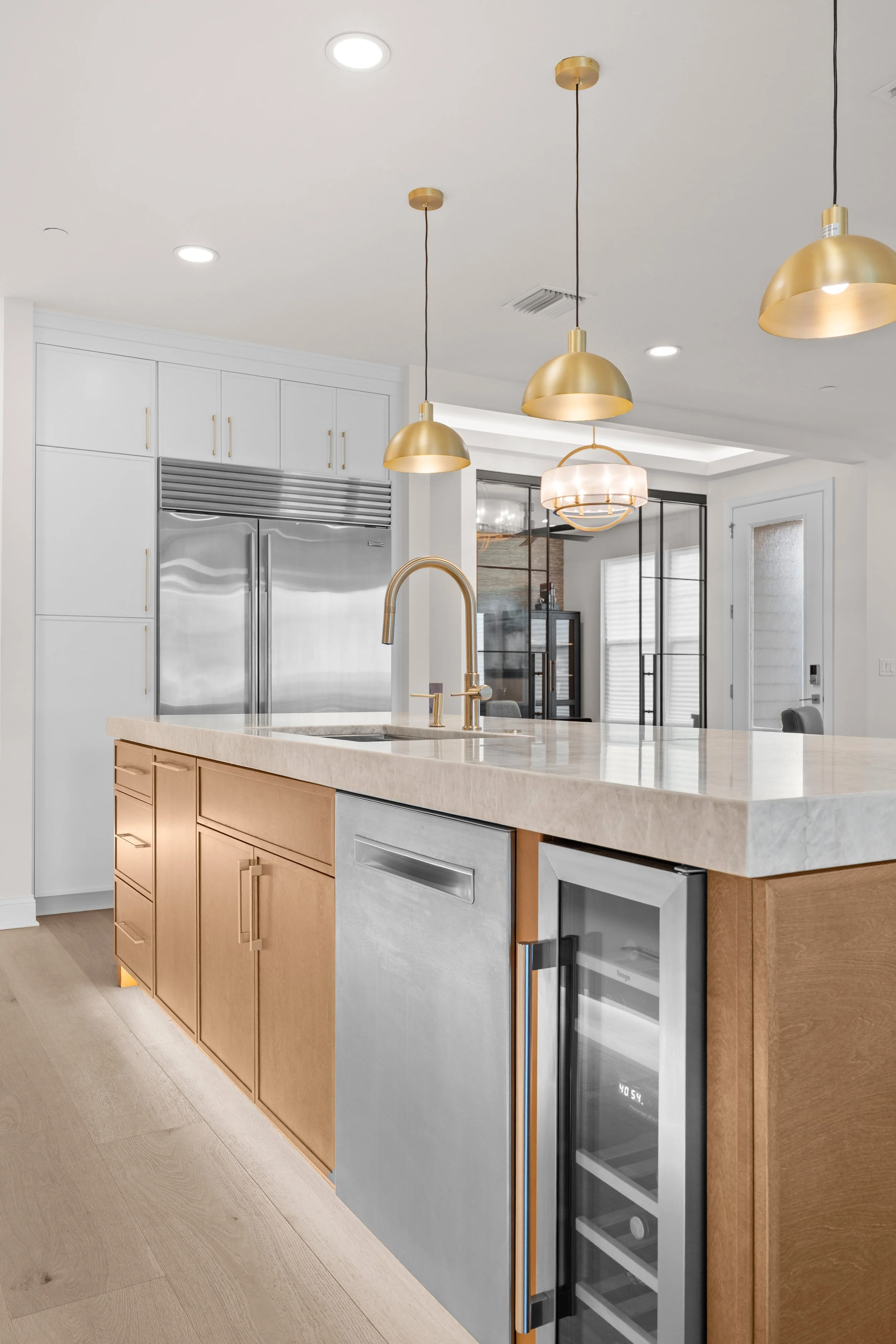 Modern kitchen with white cabinets, gold pendant lights, a marble island, and a built-in wine cooler.