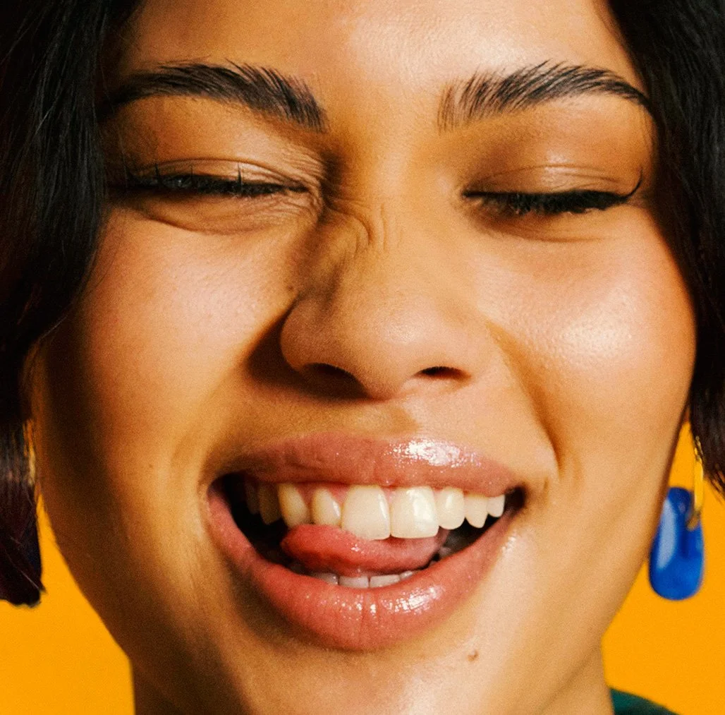 adidas Football safa world cup 2026 jersey launch Bafana Bafana athletes. Away jersey. Close-up of a woman with short dark hair, smiling with tongue out, wearing blue earrings and makeup, against a yellow background.