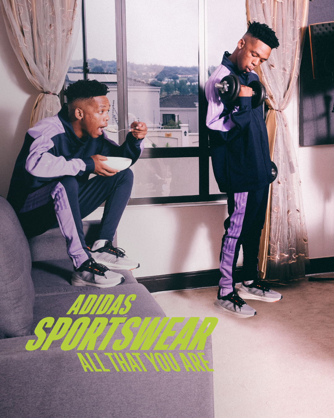 Two young men in Adidas sportswear, one sitting on a couch eating cereal and the other standing by the window lifting a dumbbell, in a living room with a window showing an outdoor view, and the words 'Adidas Sportswear All That You Are' written in green text.