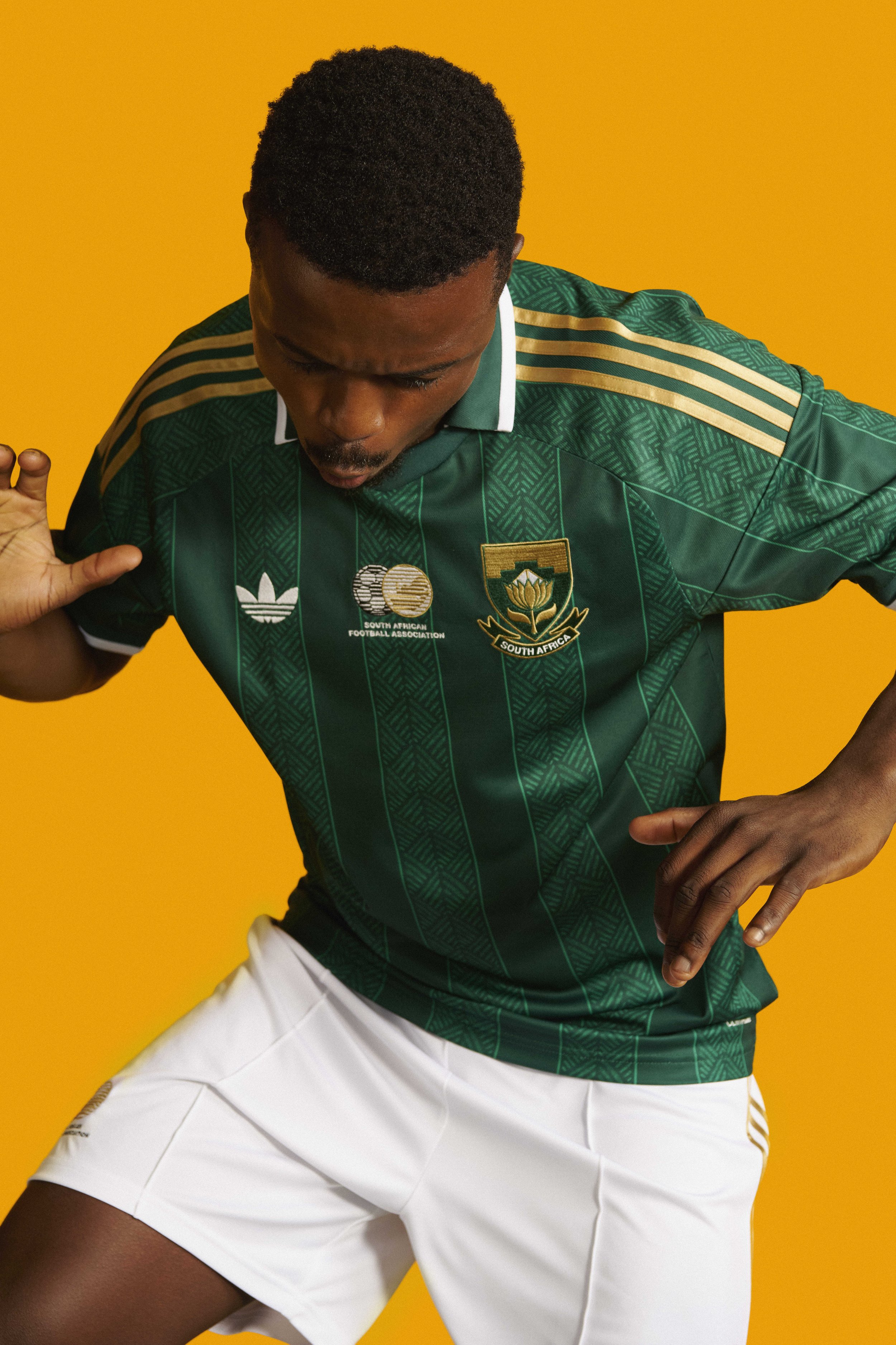 adidas Football safa world cup 2026 jersey launch Bafana Bafana athletes. Away jersey. A male athlete in a green South African soccer jersey and white shorts poses in front of a yellow background.