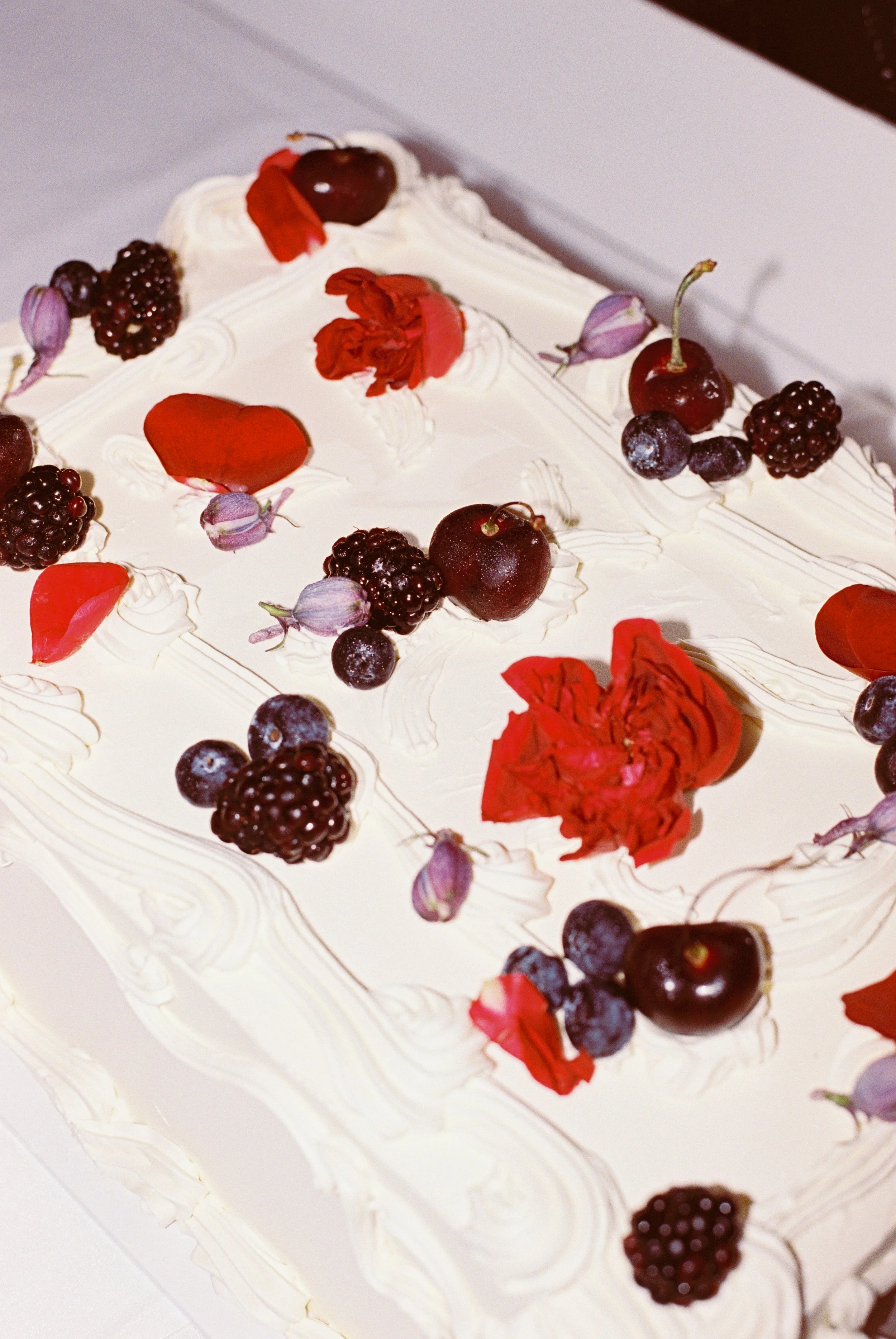 Close-up of a white birthday cake decorated with fresh cherries, blackberries, and purple flowers.