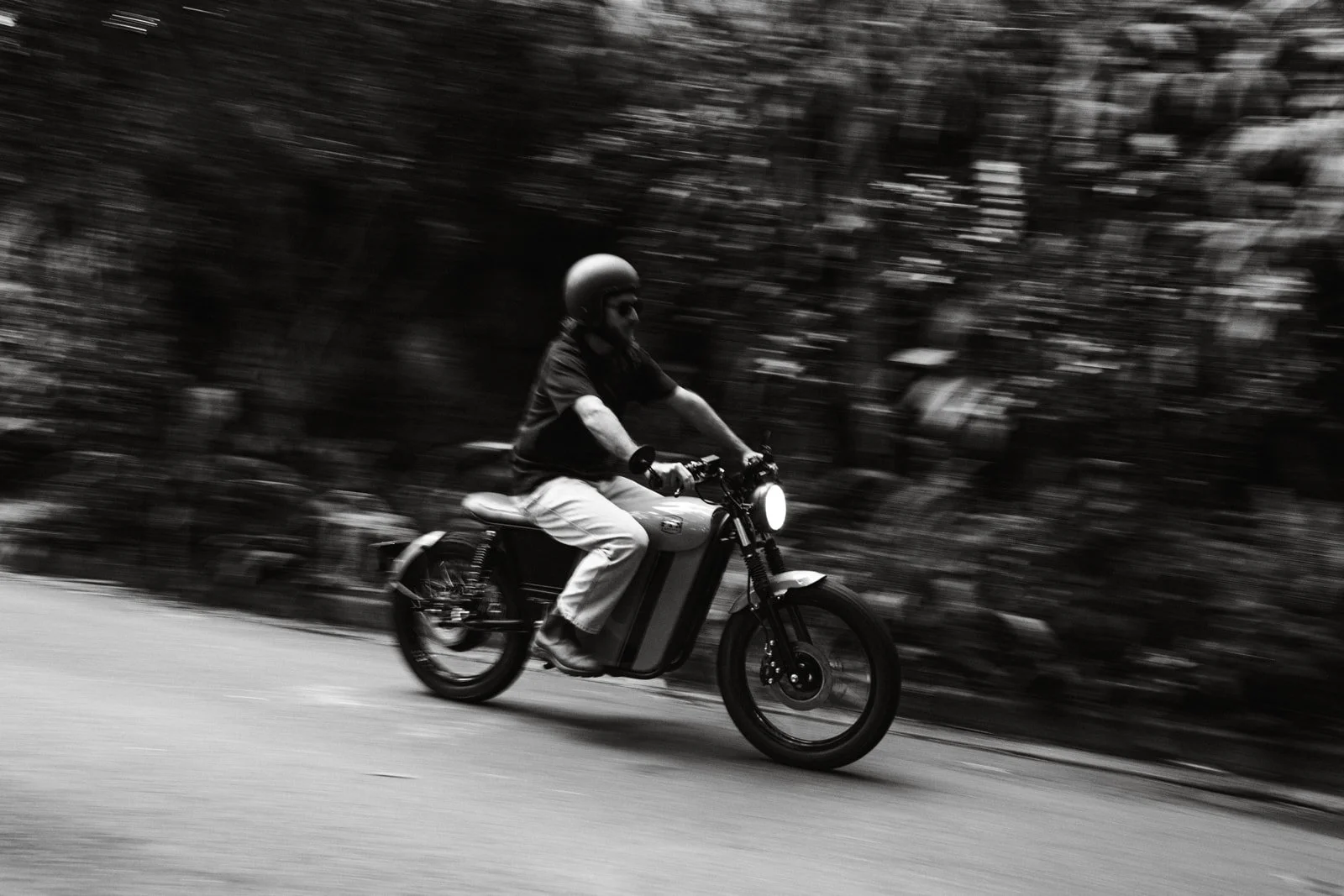 A person riding an electric bicycle on a road, wearing a helmet, captured in motion with a blurred background.